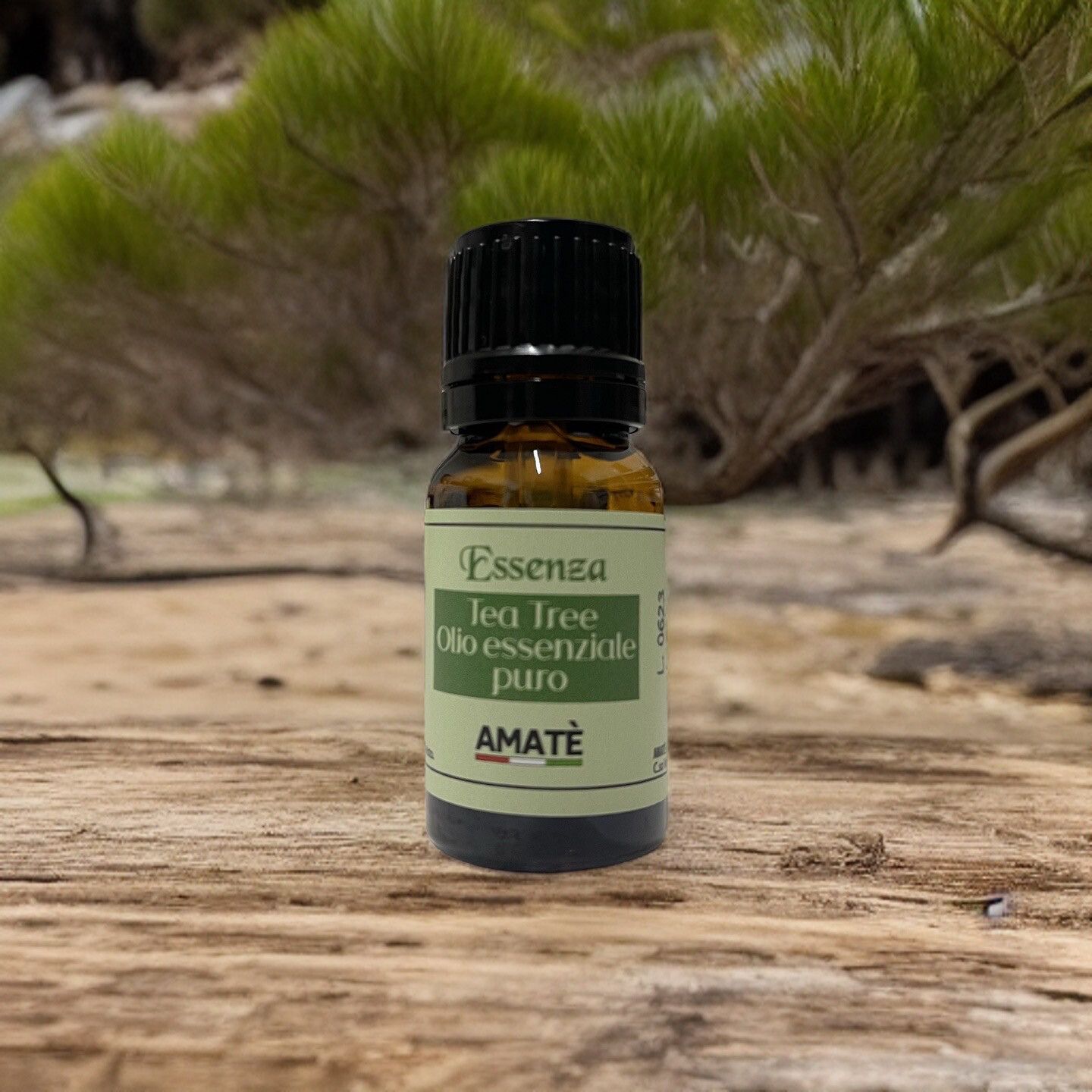 Flacone marrone con tappo nero. Etichetta: Essenza Tea Tree Olio essenziale puro. AMATÈ. Su legno, sfondo: natura.