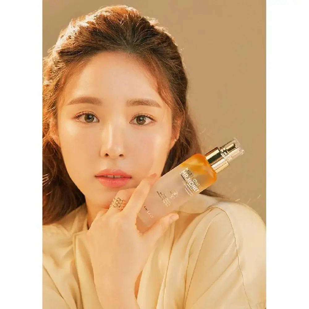 Donna tiene spray viso. Erogatore dorato, flacone trasparente con liquido giallo. Scritta: Miss Flower & Mr. Honey.