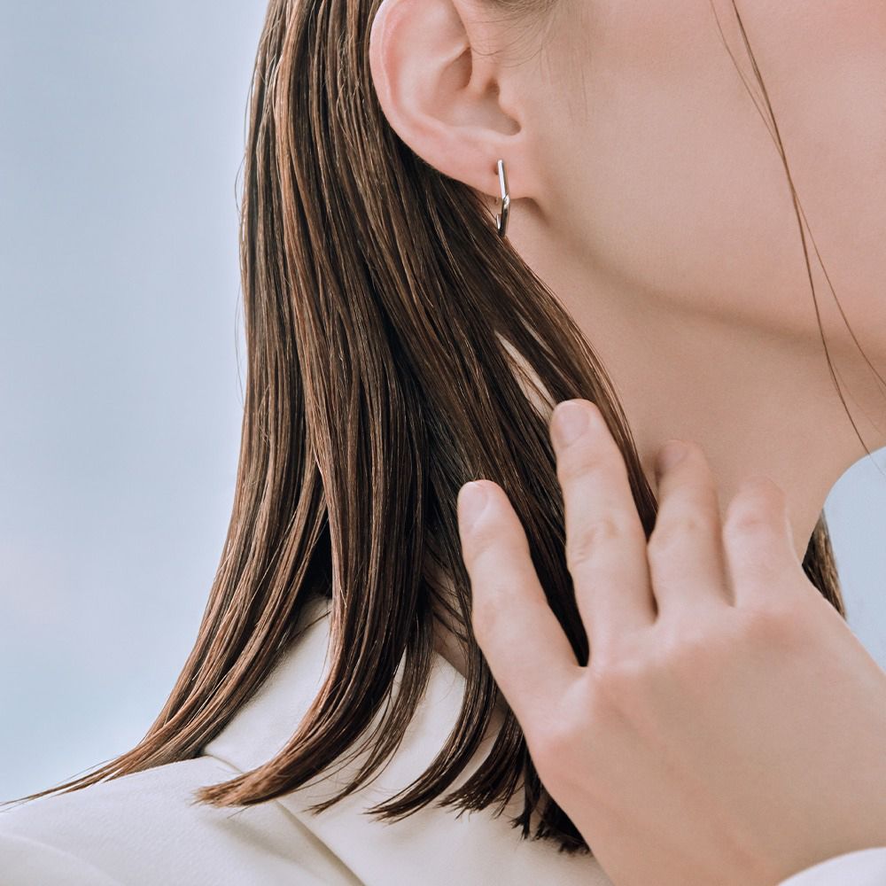 Primo piano di una persona che tocca i suoi capelli bagnati. Visibile: orecchino, consistenza dei capelli.