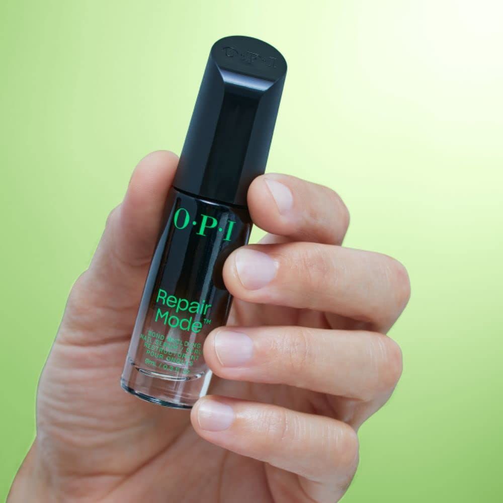 Mano che tiene il siero per unghie OPI Repair Mode. Flacone nero con scritta verde. Logo OPI.