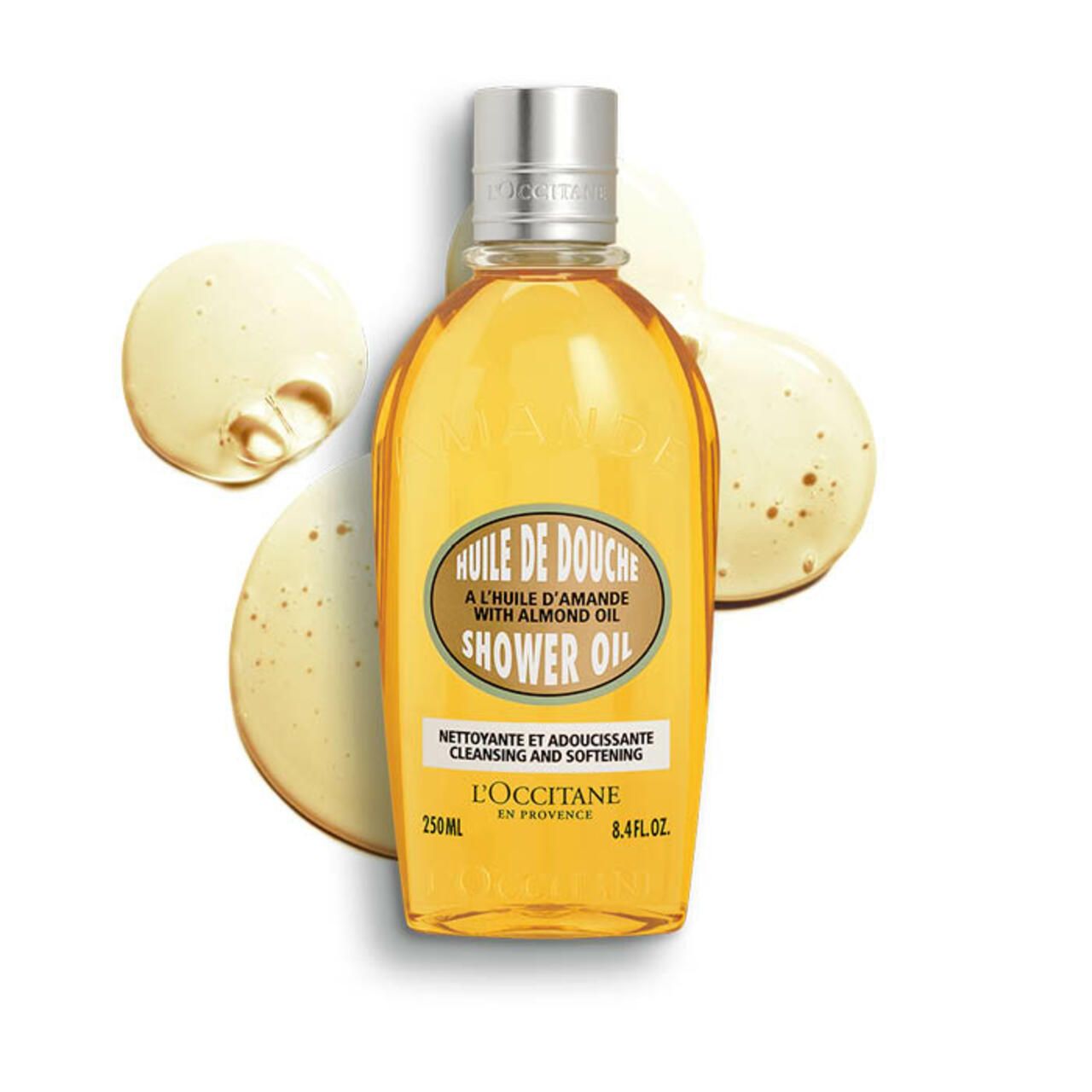 Flacone di olio doccia con schizzi. Flacone ovale, tappo argentato. Scritta: Huile de Douche, olio di mandorle, 250ml, L'Occitane.