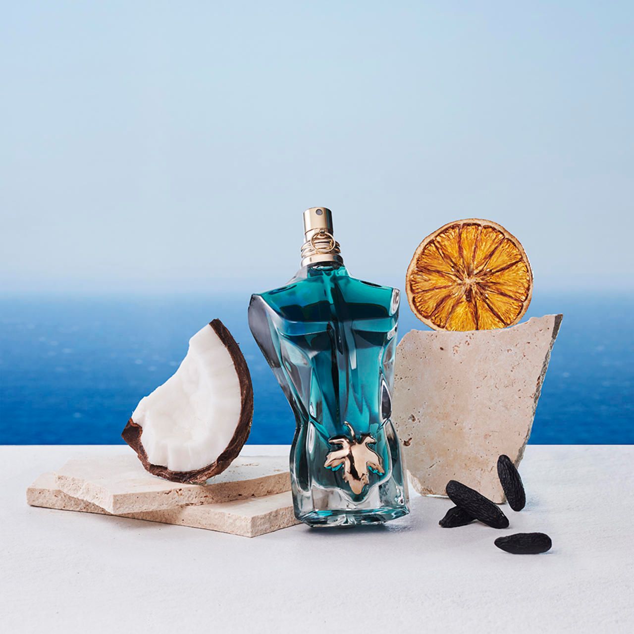 Flacone blu a forma di torso, tappo dorato, su lastre di pietra, con cocco, arancia e semi.