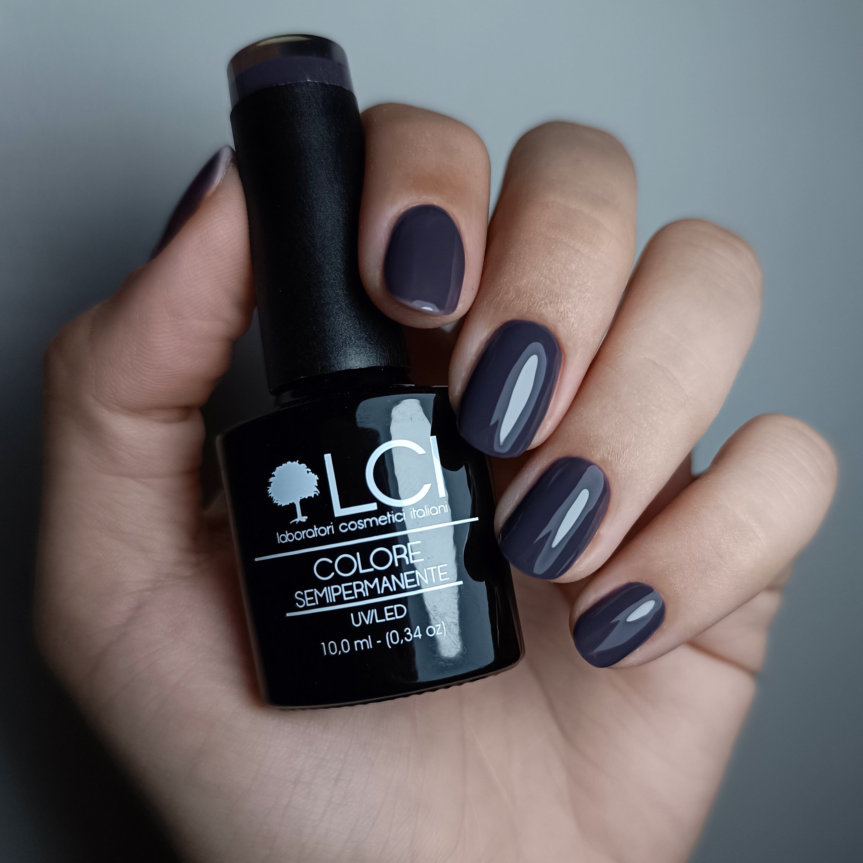 Mano che tiene flacone smalto e mostra unghie smaltate di grigio. Scritta: LCI, Colore Semipermanente, UVLED 10,0 ml.