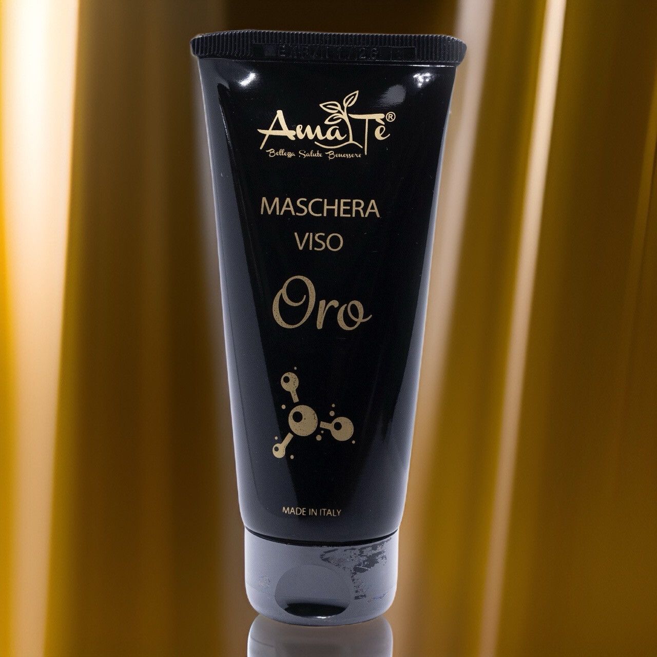 Tubo nero con testo dorato. Scritta: Amatè, Maschera Viso, Oro. Prodotto in Italia. Su sfondo dorato.