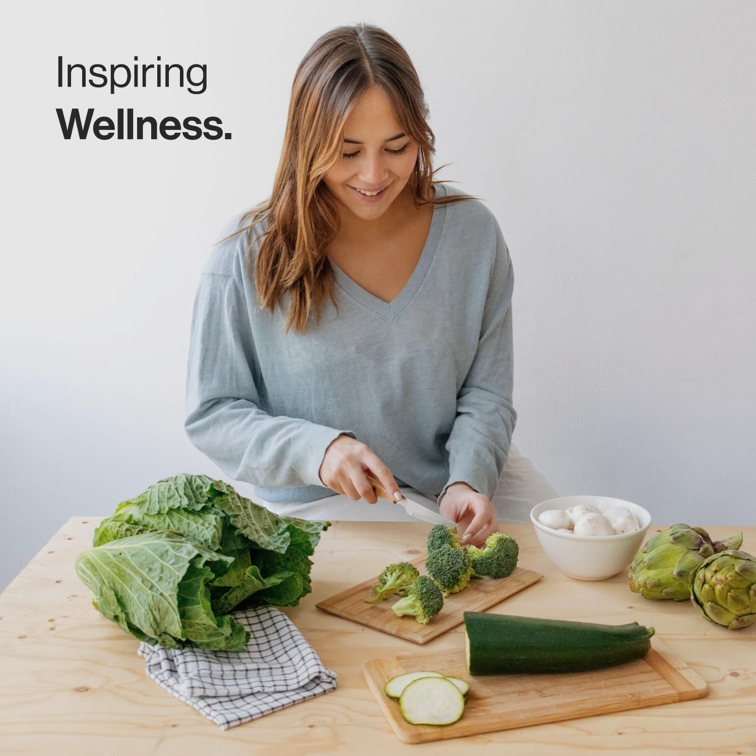Donna che taglia verdure su un tagliere di legno. Sul tavolo: broccoli, zucchine, cavolo, carciofi e funghi.