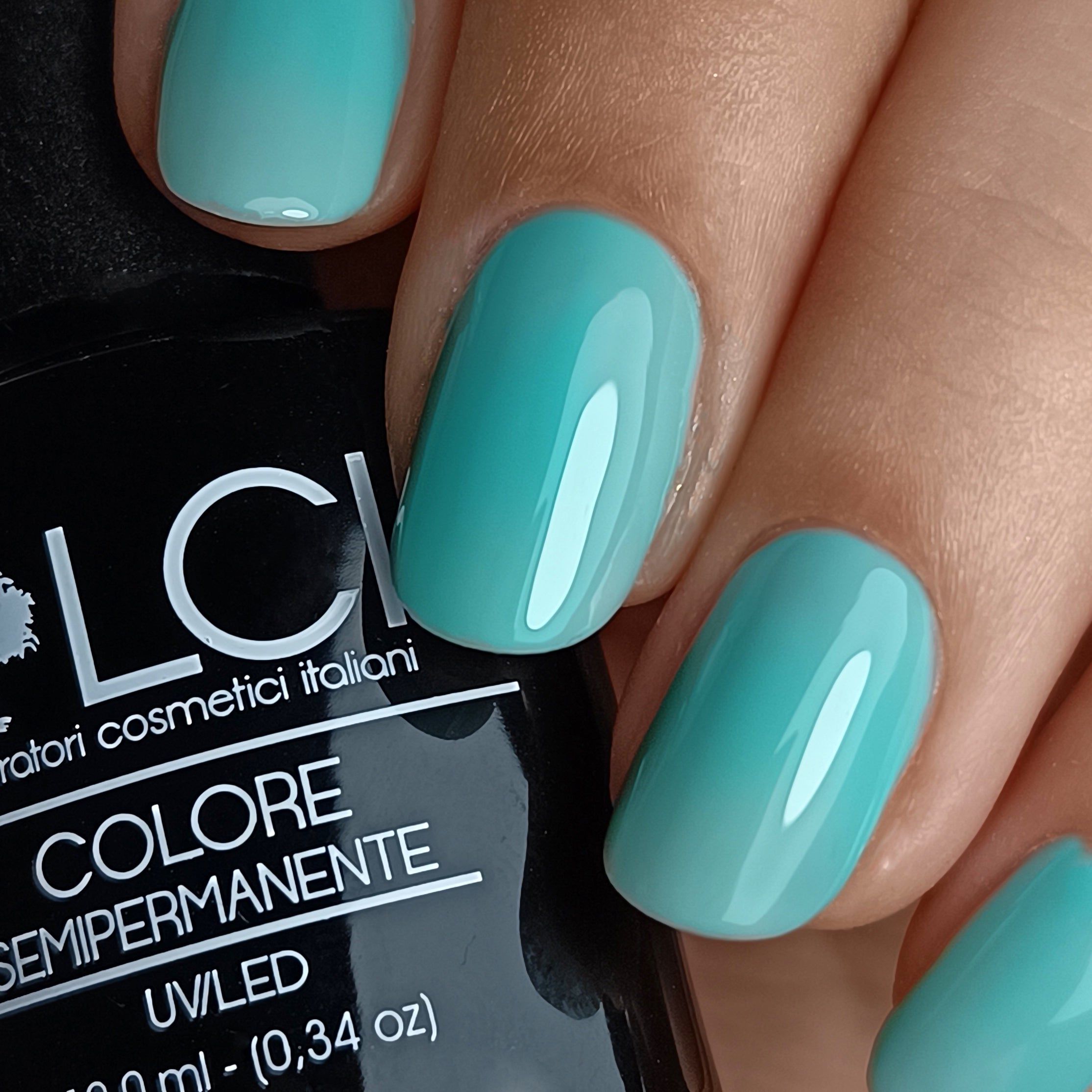 Unghie smaltate con smalto verde menta. Flacone con testo sullo sfondo. Primo piano delle unghie smaltate.