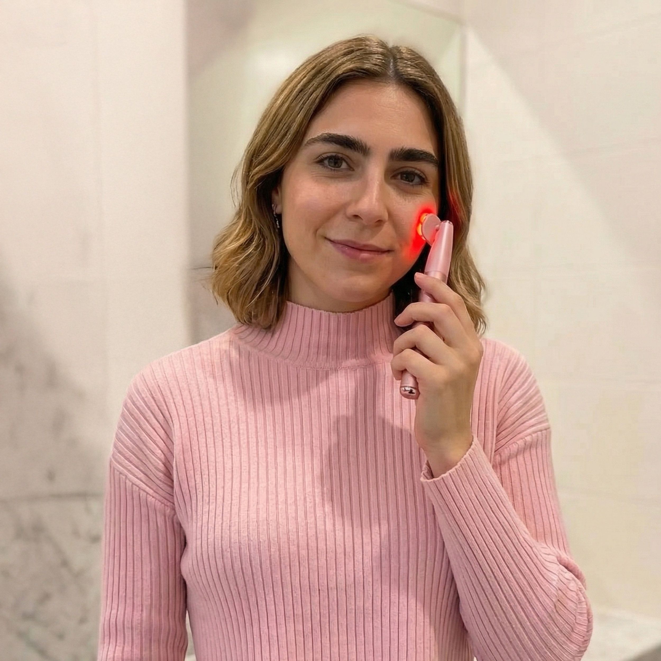 Persona tiene dispositivo rosa per la cura della pelle. Luce rossa sulla pelle. Dispositivo con manico allungato.