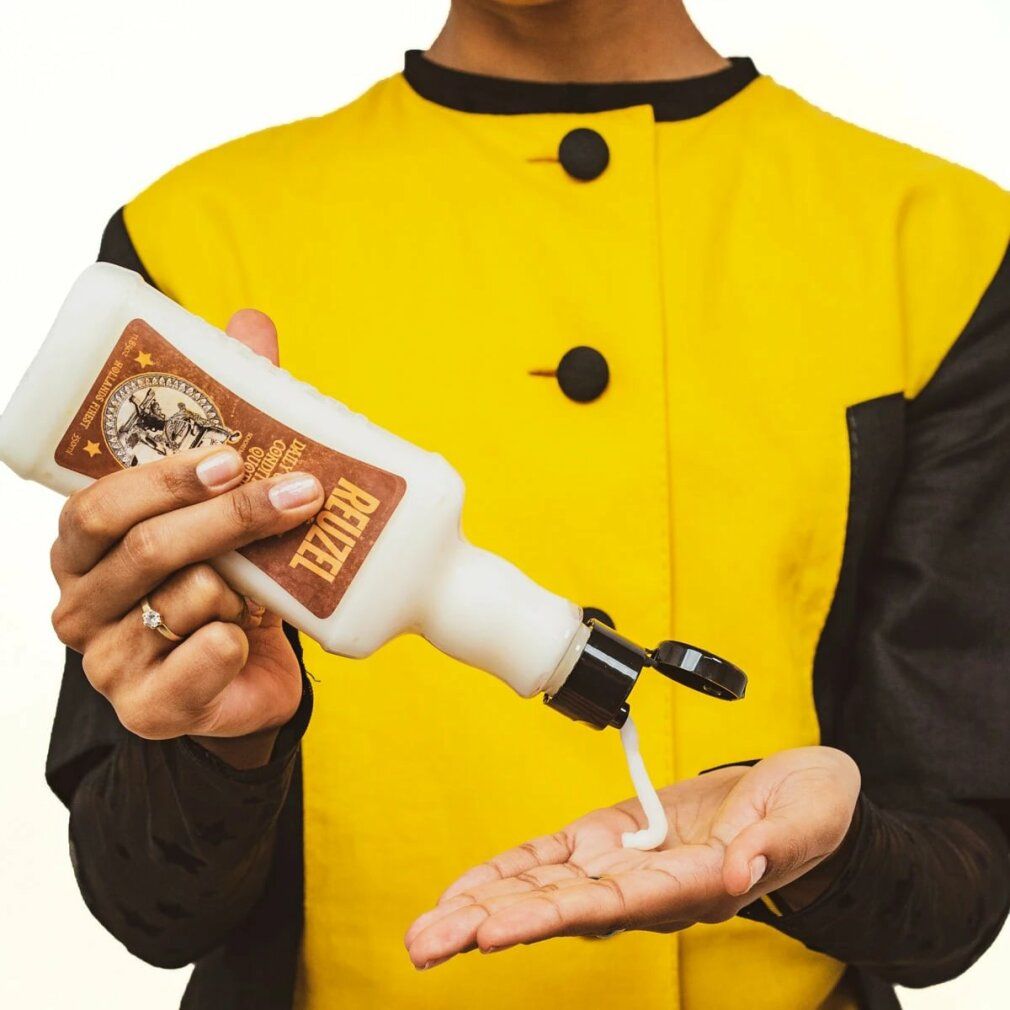 Persona tiene flacone e versa prodotto nella mano. Flacone con "Reuzel".