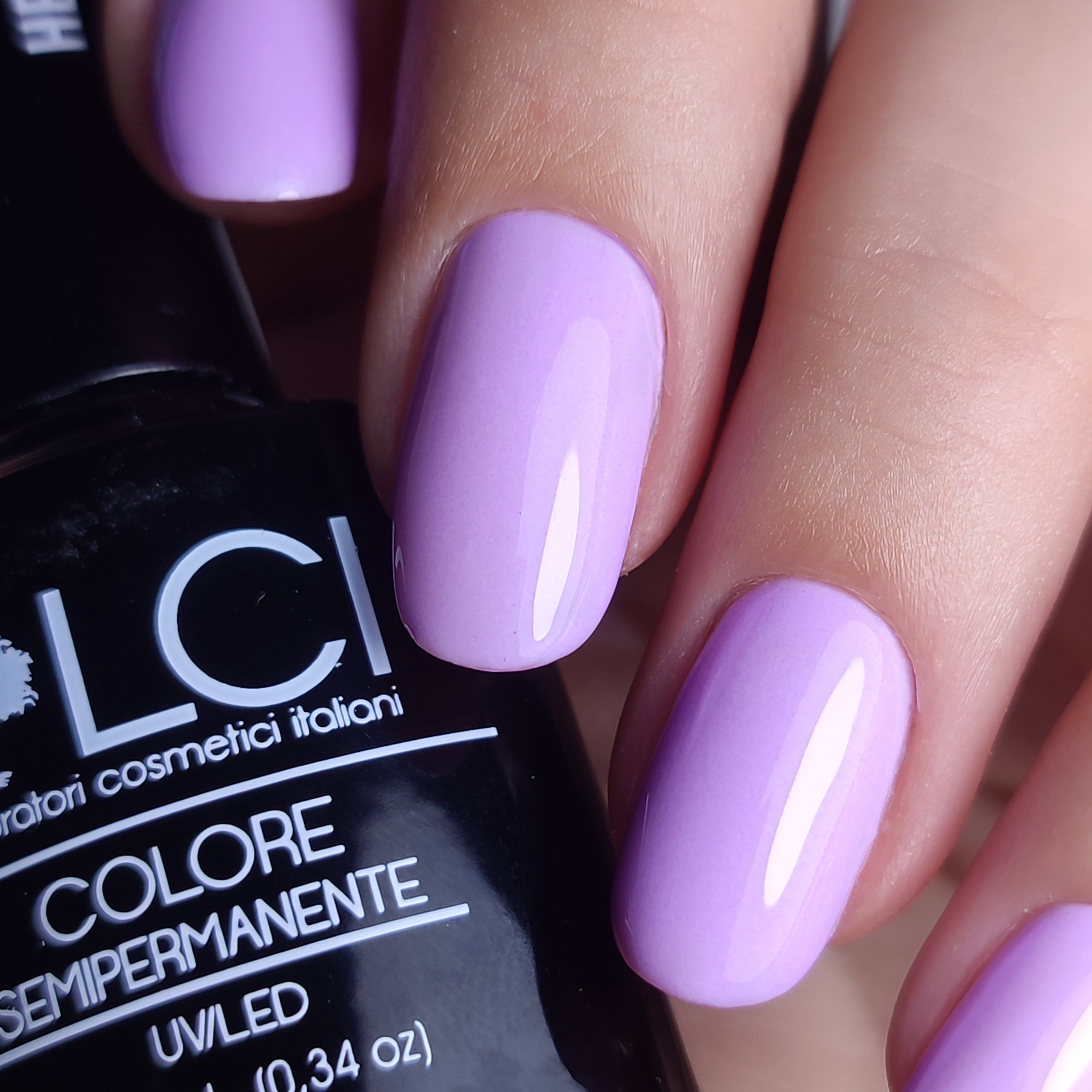 Mano con unghie smaltate di viola. Flacone di smalto sullo sfondo. Scritta: LCI, COLORE SEMIPERMANENTE.