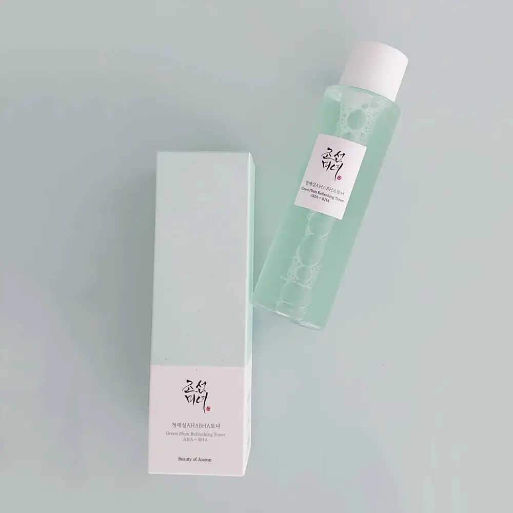 Flacone di toner e scatola su sfondo blu. Flacone: toner verde, tappo bianco, etichetta. Scatola: bianca, testo.