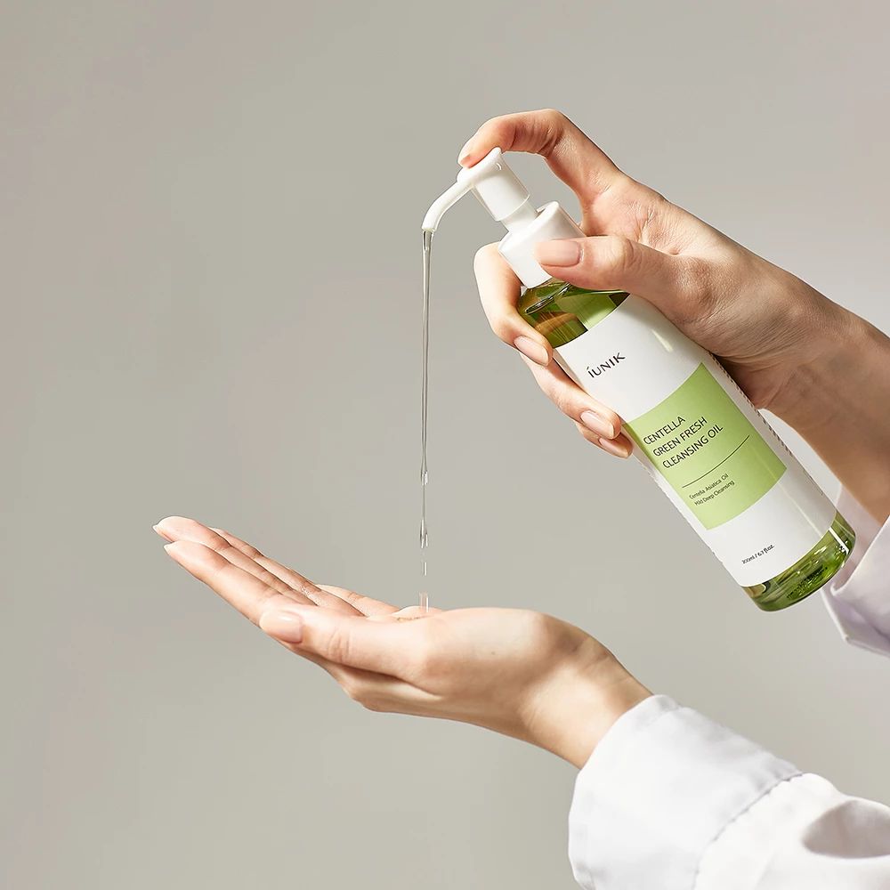 Una mano tiene un flacone con erogatore, da cui fuoriesce olio verde. Scritta: CENTELLA GREEN FRESH CLEANSING OIL, iUNIK.