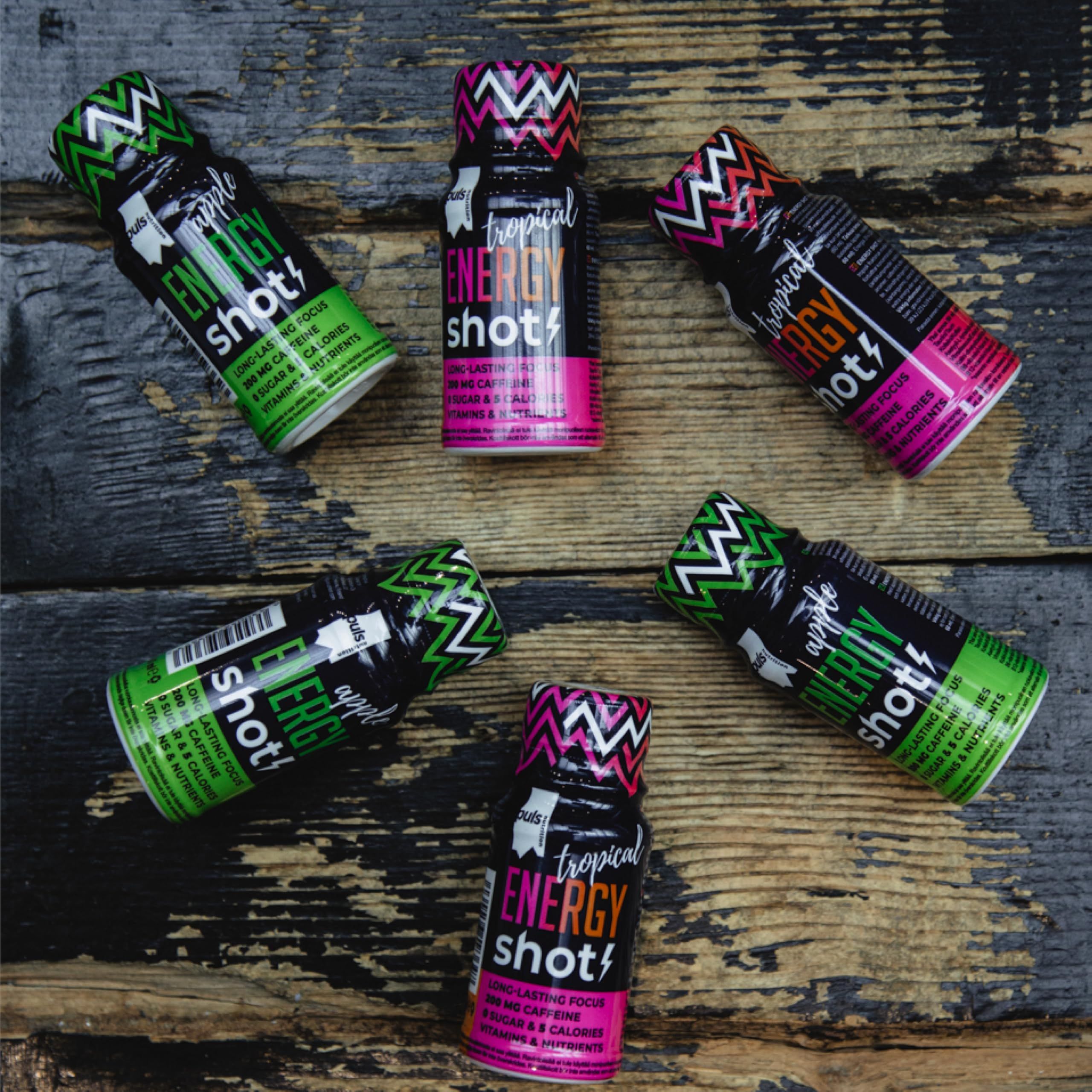 Cinque Energy Shot Puls Nutrition Mela e due Tropical Energy Shot su sfondo di legno.
