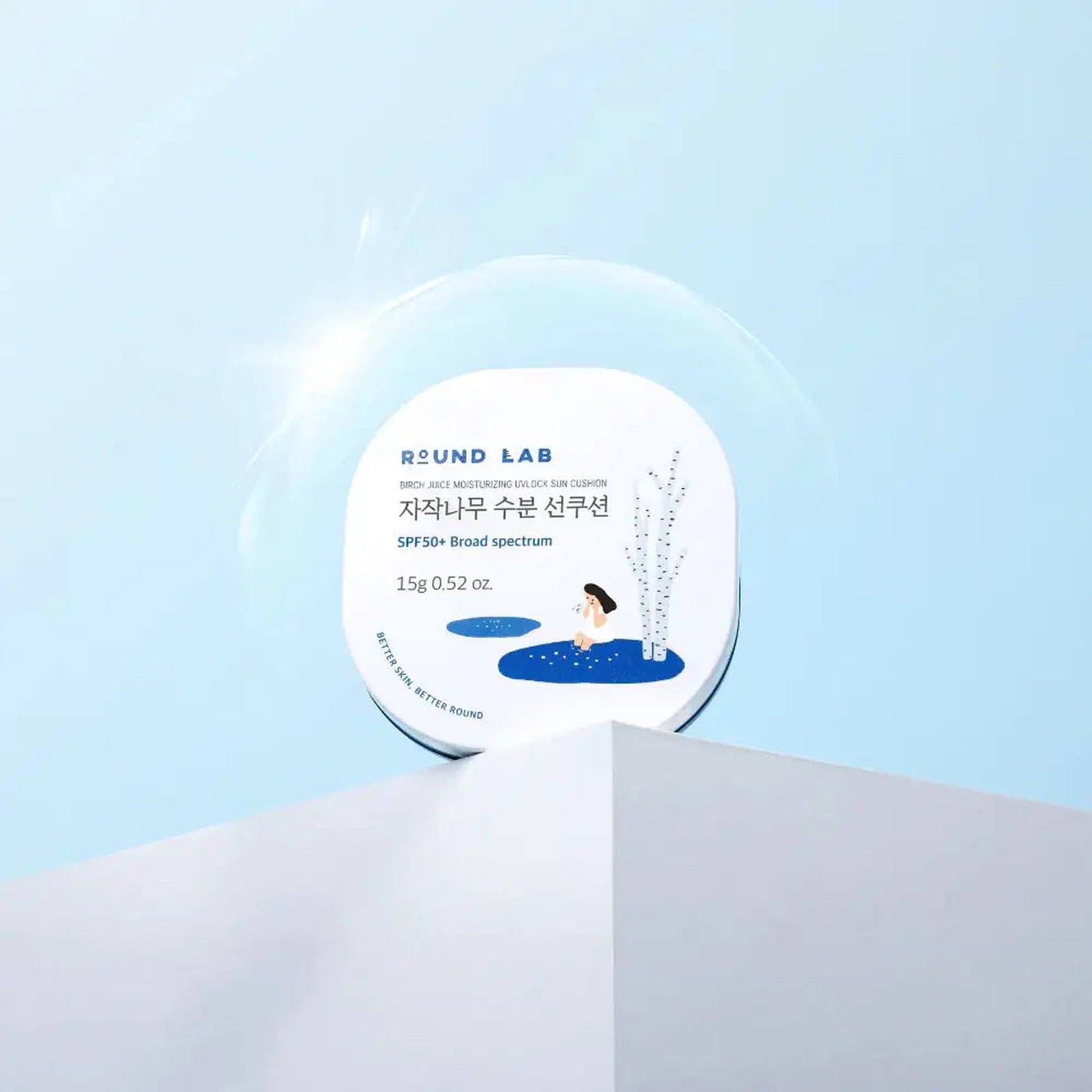 Cuscino solare Round Lab con linfa di betulla, SPF 50. Contenitore bianco con illustrazione, su piedistallo bianco.