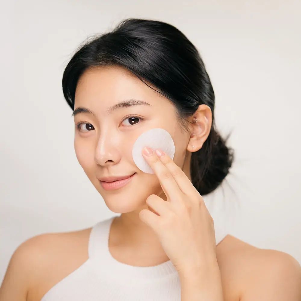 Donna con un dischetto di cotone sulla pelle. Tocca il viso con il dischetto.