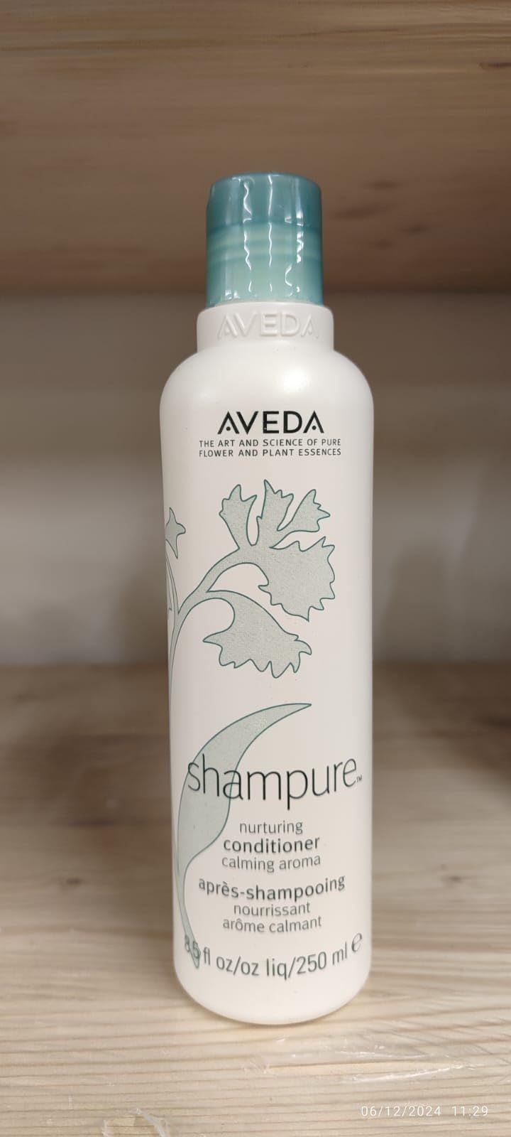 Flacone bianco con tappo blu. Scritta: Aveda, Shampure, Nurturing Conditioner. Su mensola di legno.