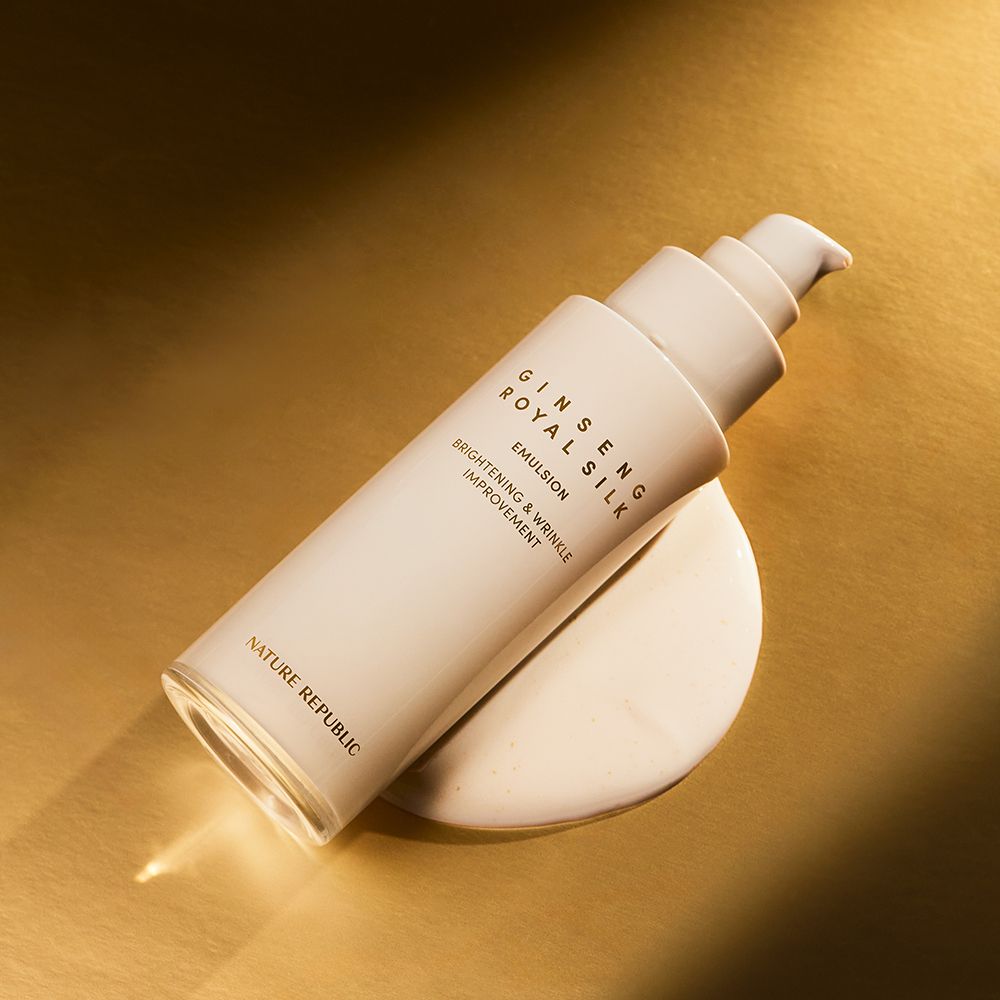 Flacone beige con dosatore, Ginseng Royal Silk Emulsion. Testo: Brightening & Wrinkle Improvement. Marchio: NATURE REPUBLIC. Su sfondo dorato.