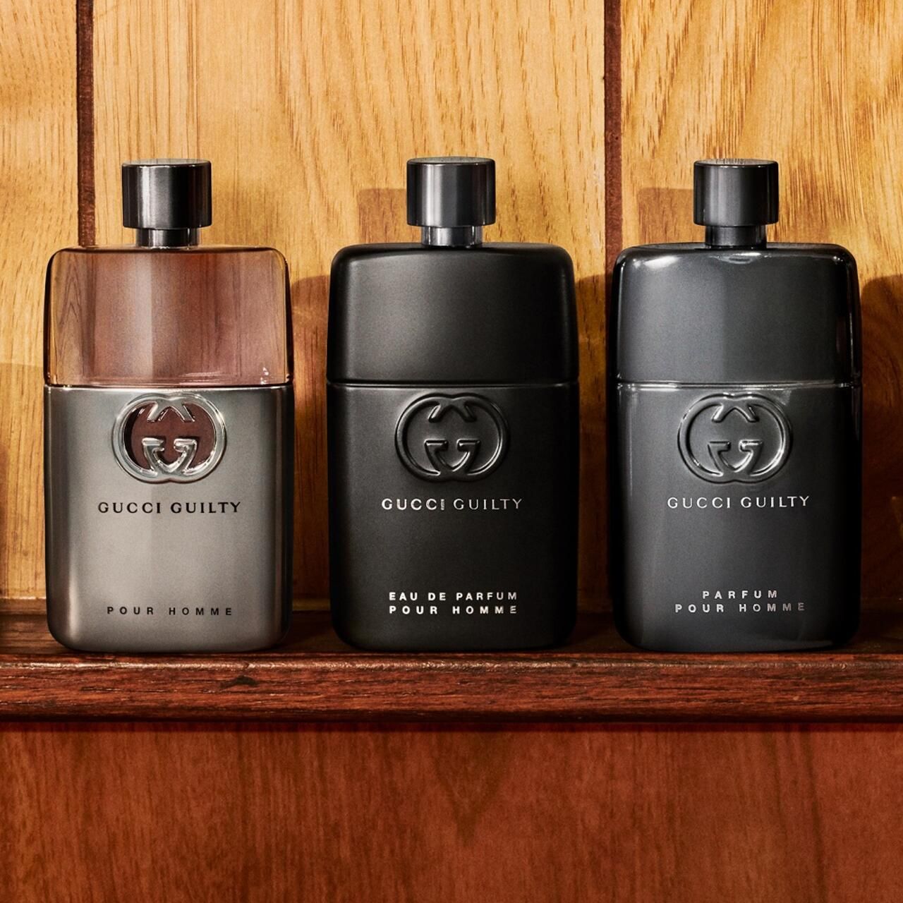 Tre flaconi. Gucci Guilty Pour Homme. Logo argentato. Sfondo in legno.