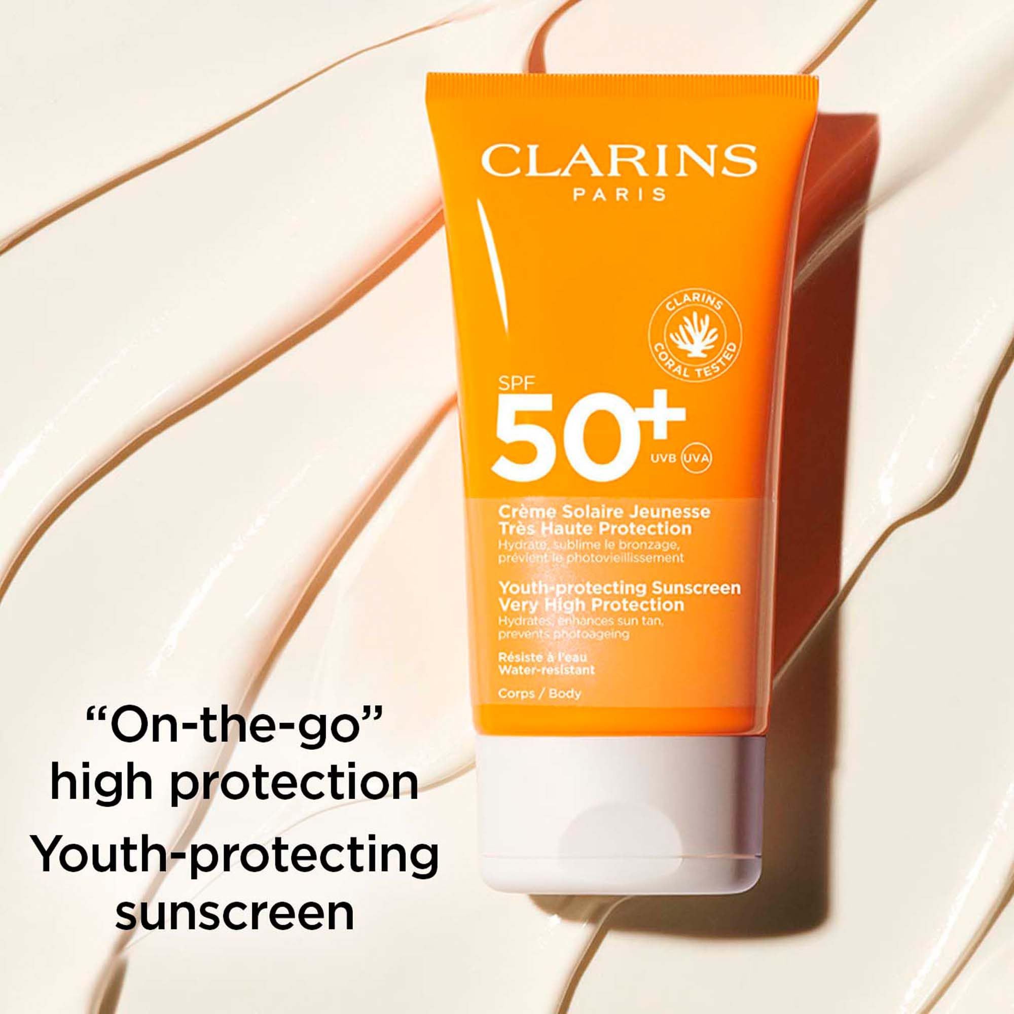 Tubo arancione di crema solare SPF 50+. Logo Clarins Paris. Testo: Crème Solaire Jeunesse. Protezione molto alta. Testato corallo.