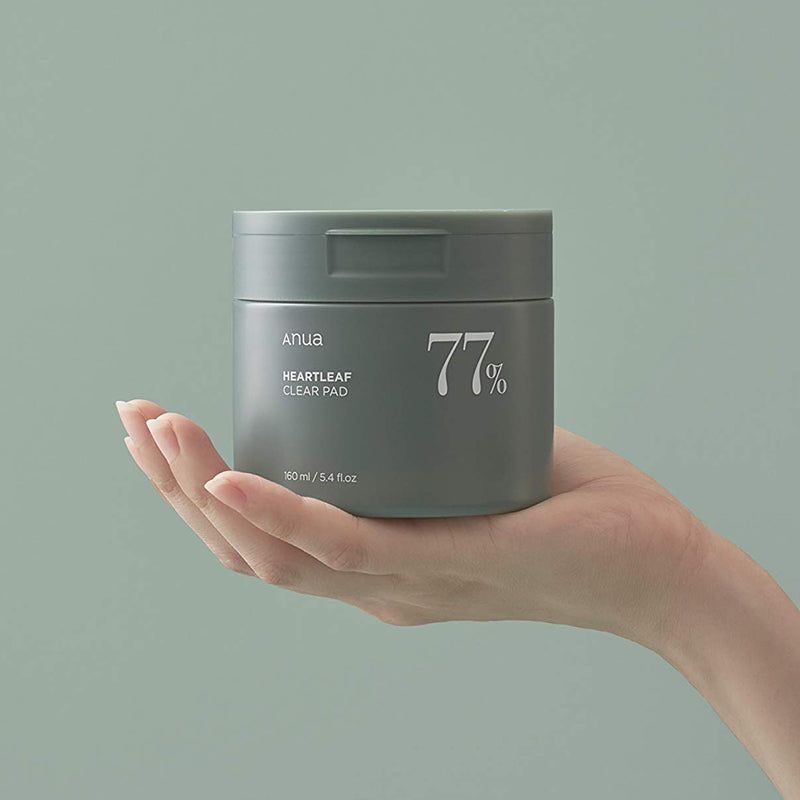 Mano che tiene un barattolo verde. Scritta: Anua, HEARTLEAF CLEAR PAD, 77%.