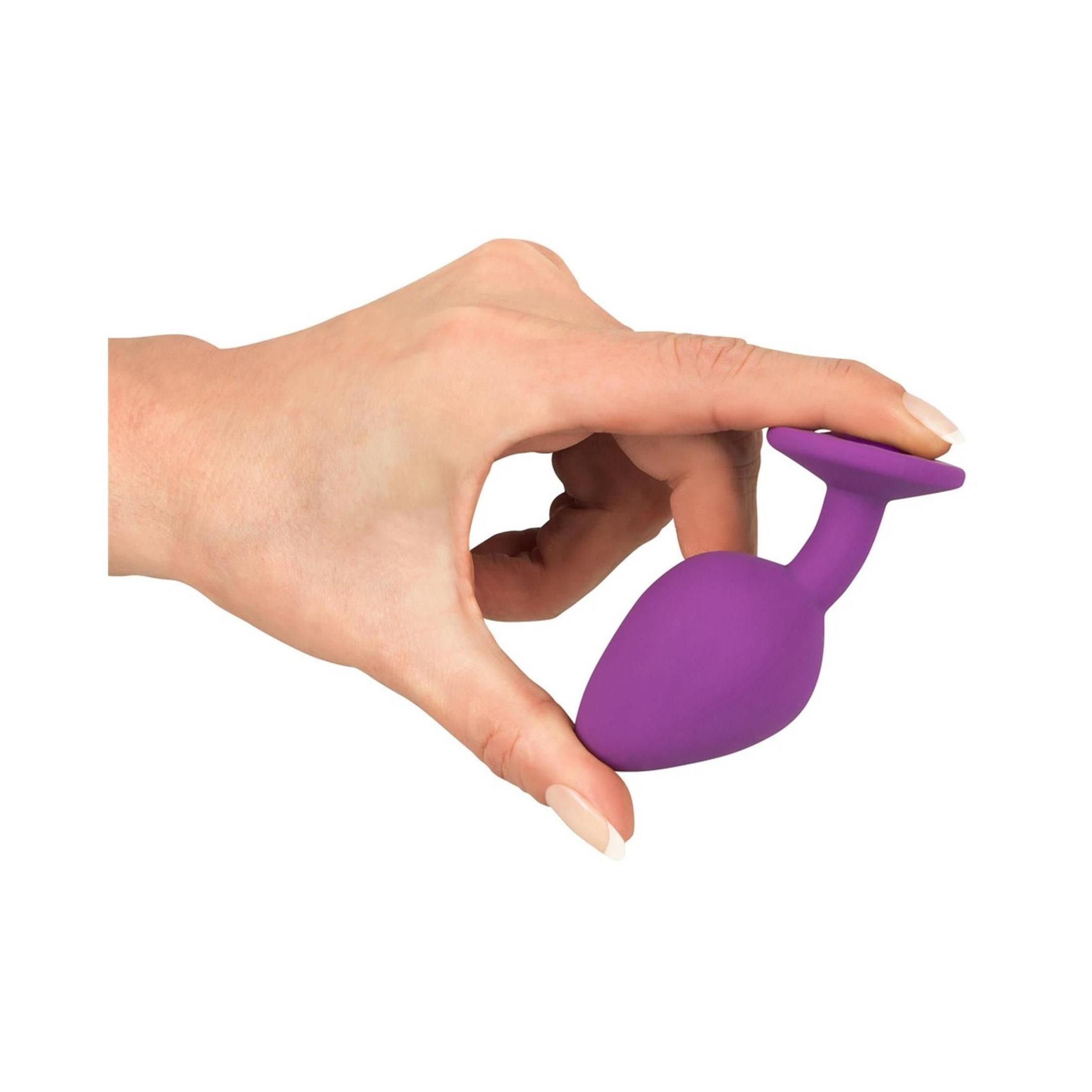 Mano che tiene un plug viola. Forma conica, base rotonda. Primo piano.