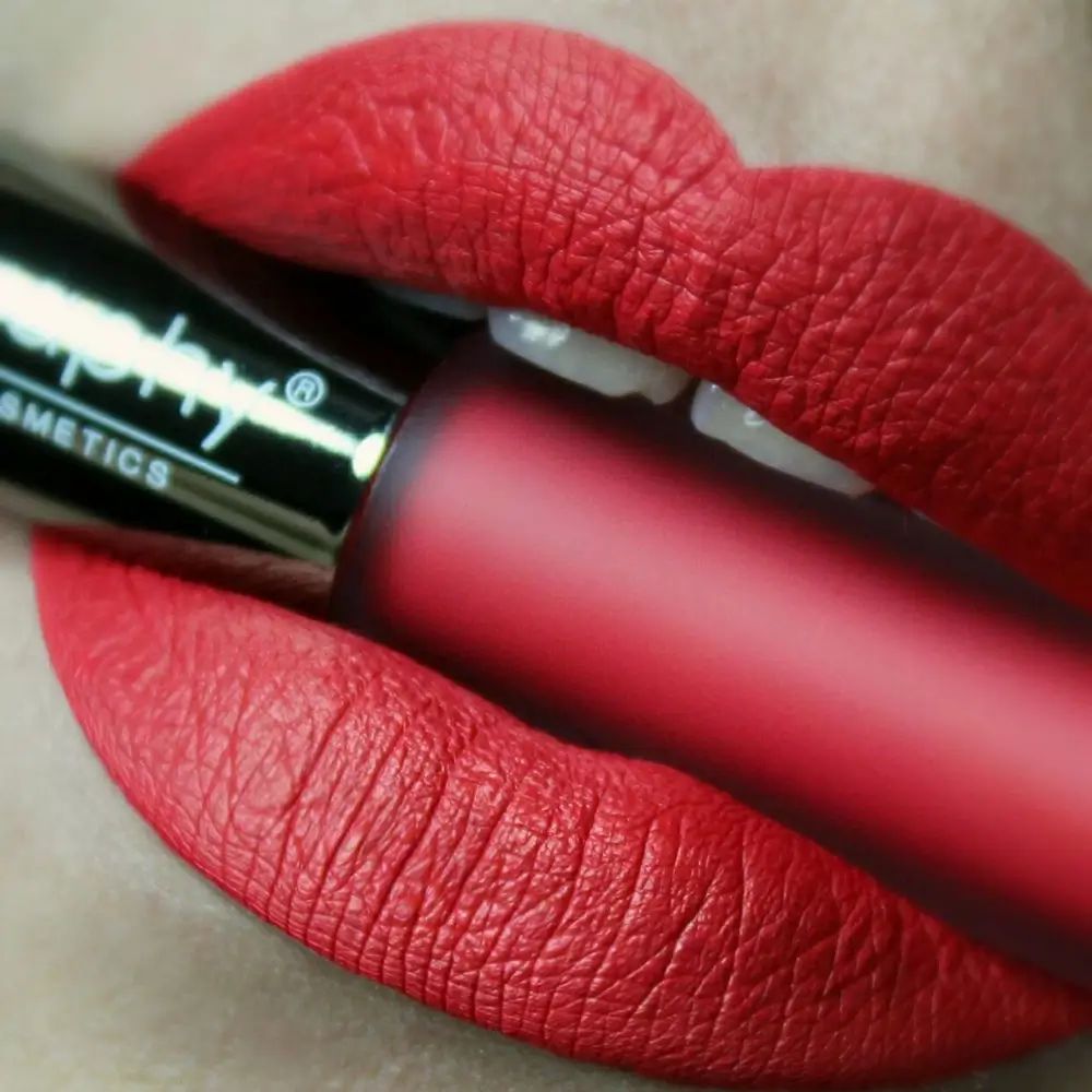 Labbra rosse con rossetto liquido BODYOGRAPHY. L'applicatore è tra le labbra. Il testo è visibile.