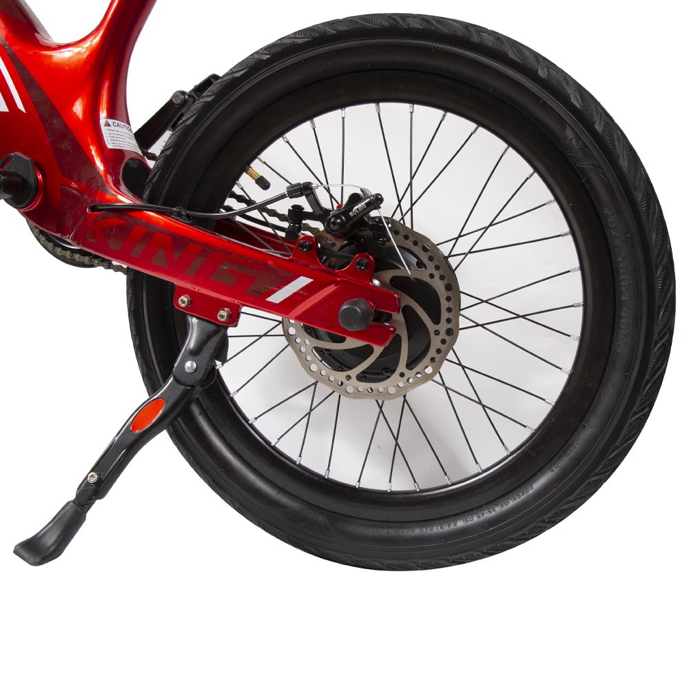 Bicicletta elettrica rossa, dettaglio ruota posteriore. Pneumatico nero, disco freno, cavalletto. Cerchio con raggi.