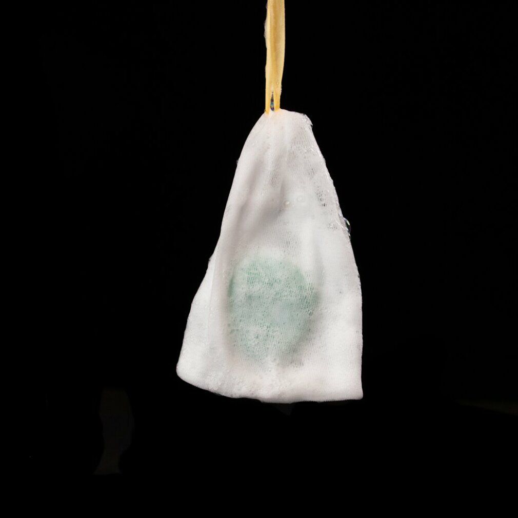 Barra shampoo verde in un sacchetto di schiuma, appesa a un filo. Sfondo nero.