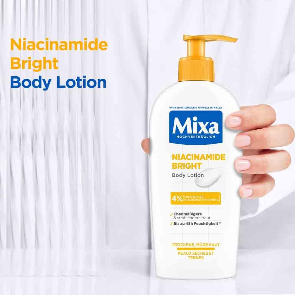 Persona tiene in mano un flacone di Mixa Niacinamide Bright Body Lotion. Erogatore giallo, flacone bianco.