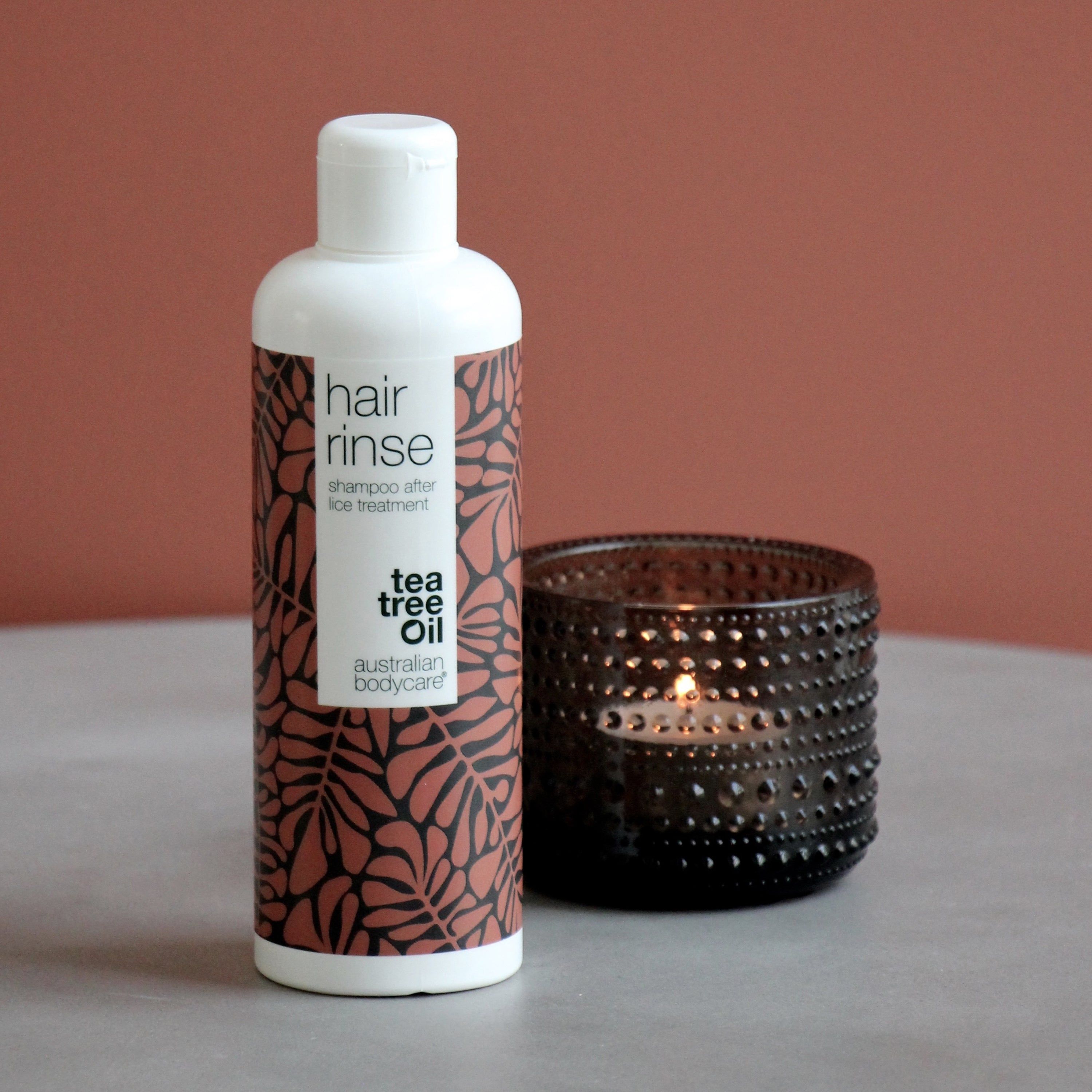 Flacone bianco. Scritta: hair rinse, shampoo after lice treatment, tea tree oil, Australian Bodycare. Accanto, una candela.