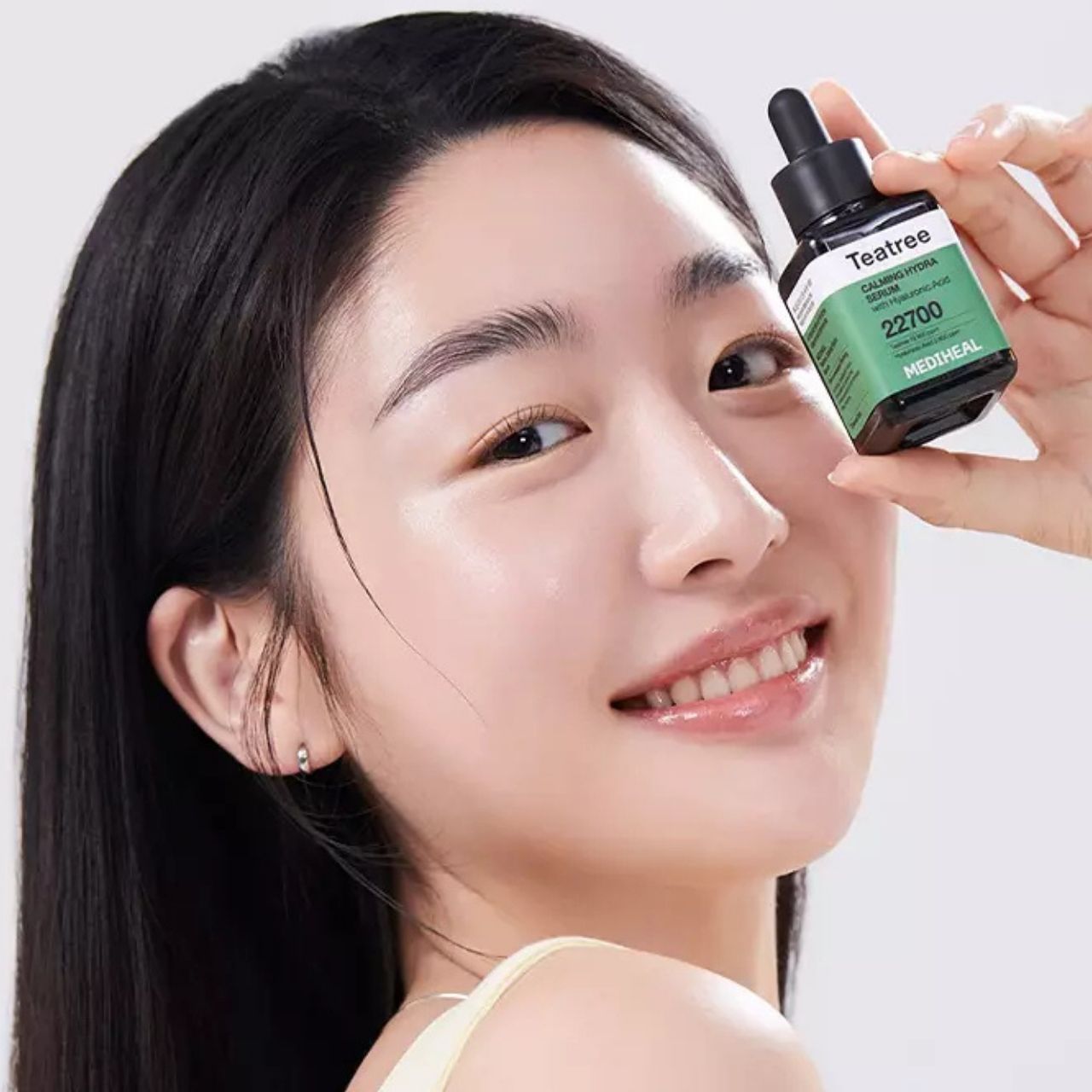 Donna che tiene una bottiglia di siero idratante lenitivo al tea tree MEDIHEAL vicino al viso.