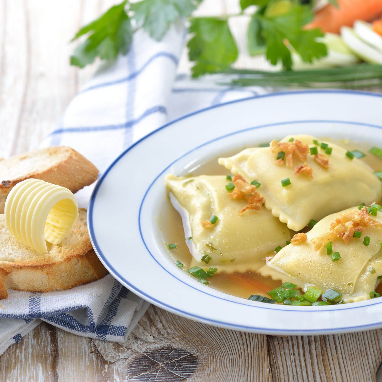 Piatto di ravioli in brodo, guarniti con erba cipollina. Con pane e burro.