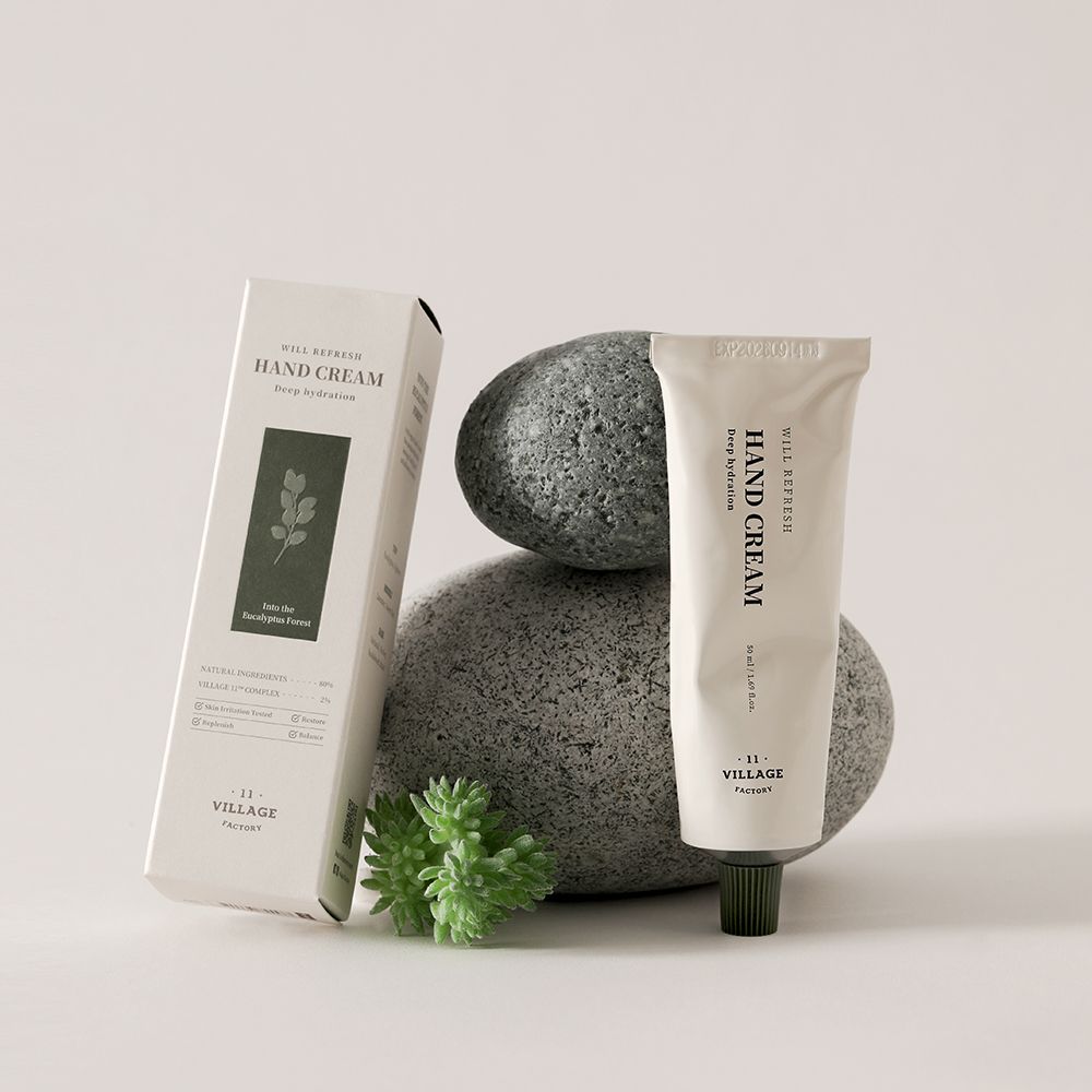 Tubetto di crema e scatola accanto a pietre. Scritta: WILL REFRESH HAND CREAM, VILLAGE 11 FACTORY. Scatola con motivo a foglie.