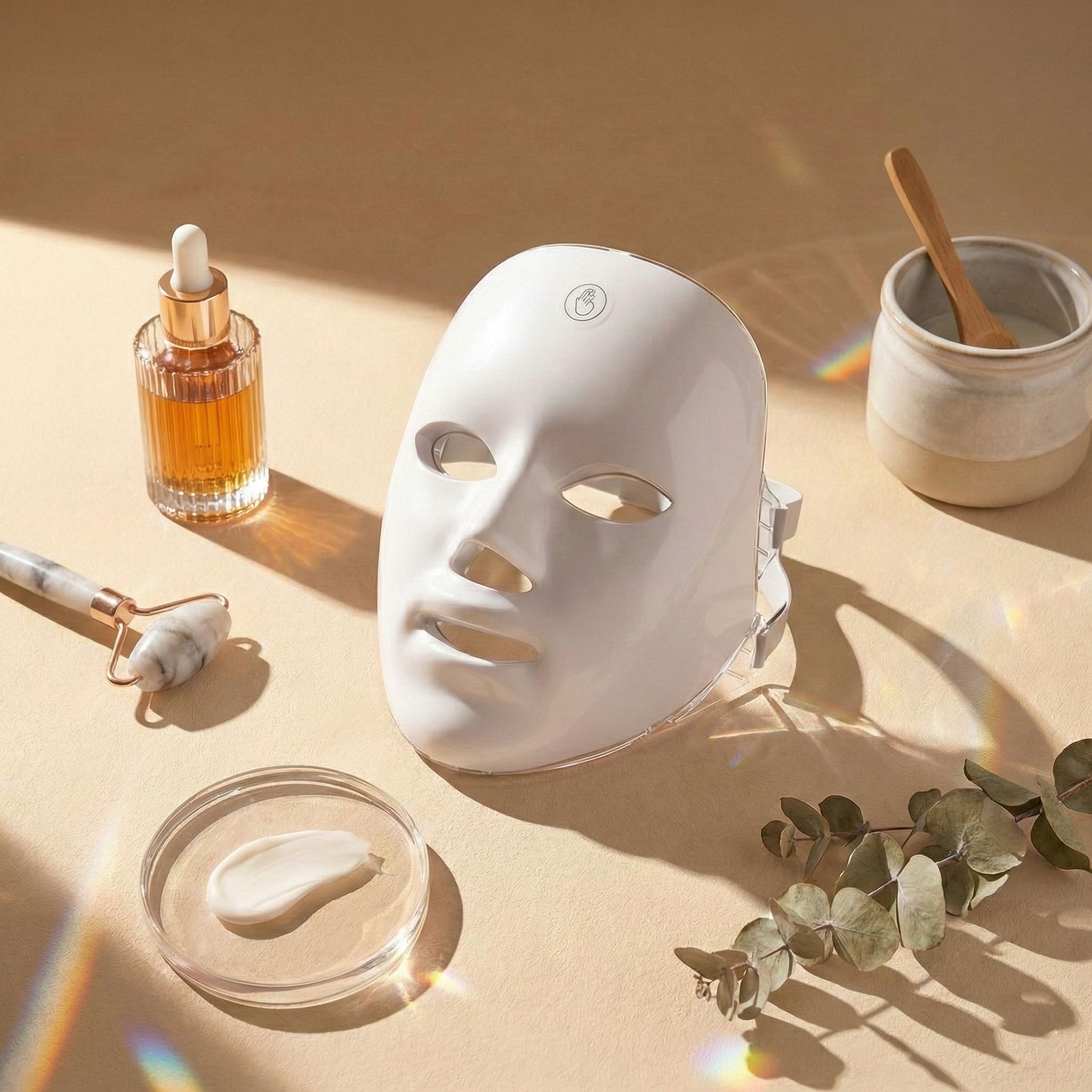 Maschera per terapia LED con prodotti per la cura della pelle come siero e rullo facciale.