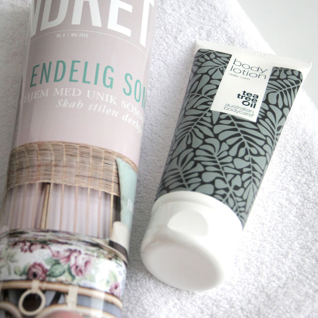 Tubo di Body Lotion accanto a una rivista. Tubo bianco con motivi a foglie grigie. Testo: Tea Tree Oil, Australian Bodycare.