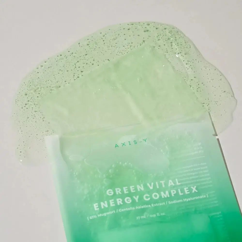 Maschera viso aperta con liquido. AXIS-Y Green Vital Energy Complex. Liquido verdastro e maschera su sfondo bianco.