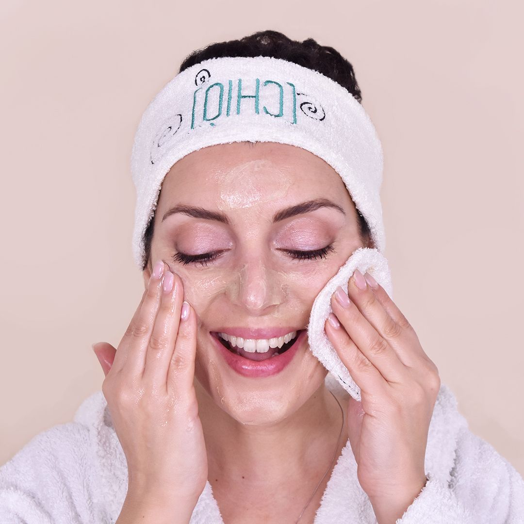 Donna con occhi chiusi, pulisce il viso con un dischetto. Fascia con logo.