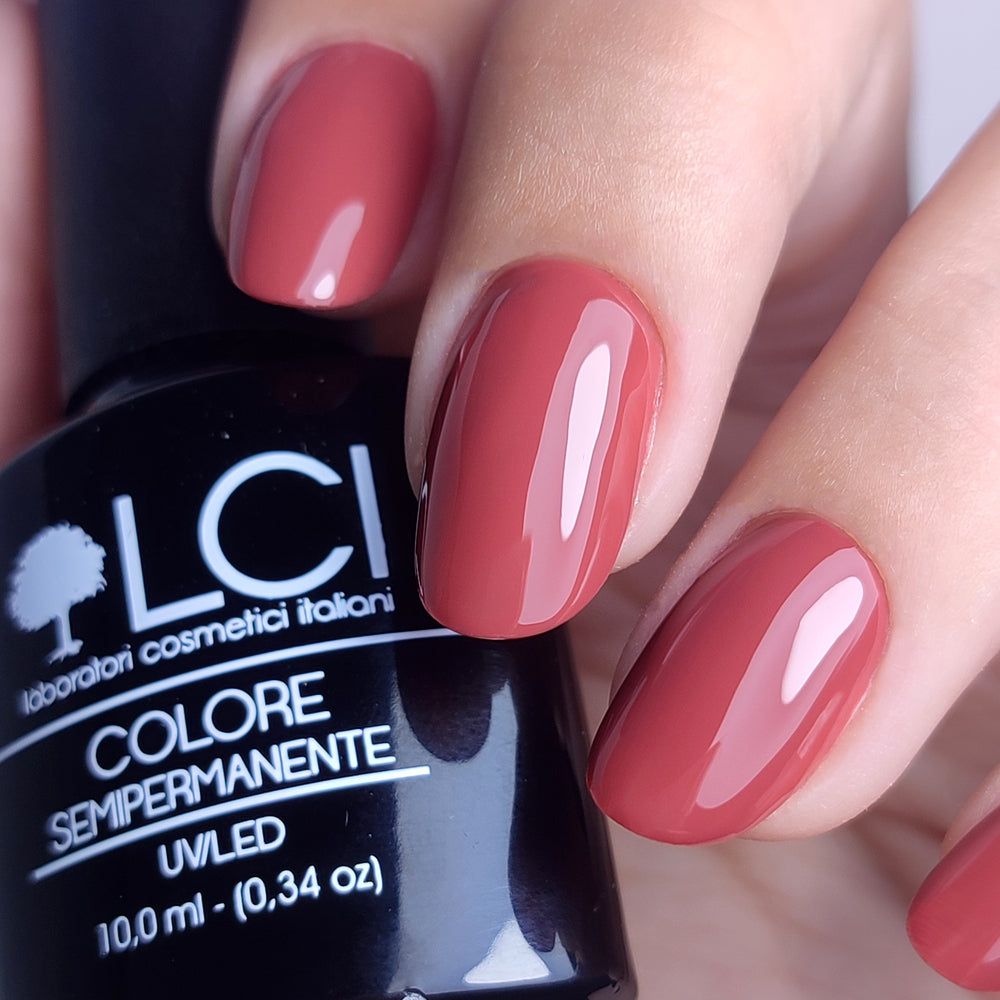 Primo piano di unghie smaltate e flacone di smalto. LCI Cosmetics, smalto semipermanente, colore Rosso. Flacone nero.