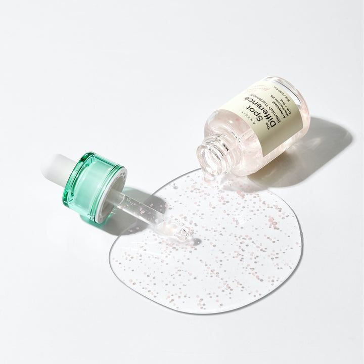 Flacone del prodotto sdraiato, liquido che fuoriesce. Pipetta accanto. Piccole sfere rosa sulla superficie. Sfondo bianco.