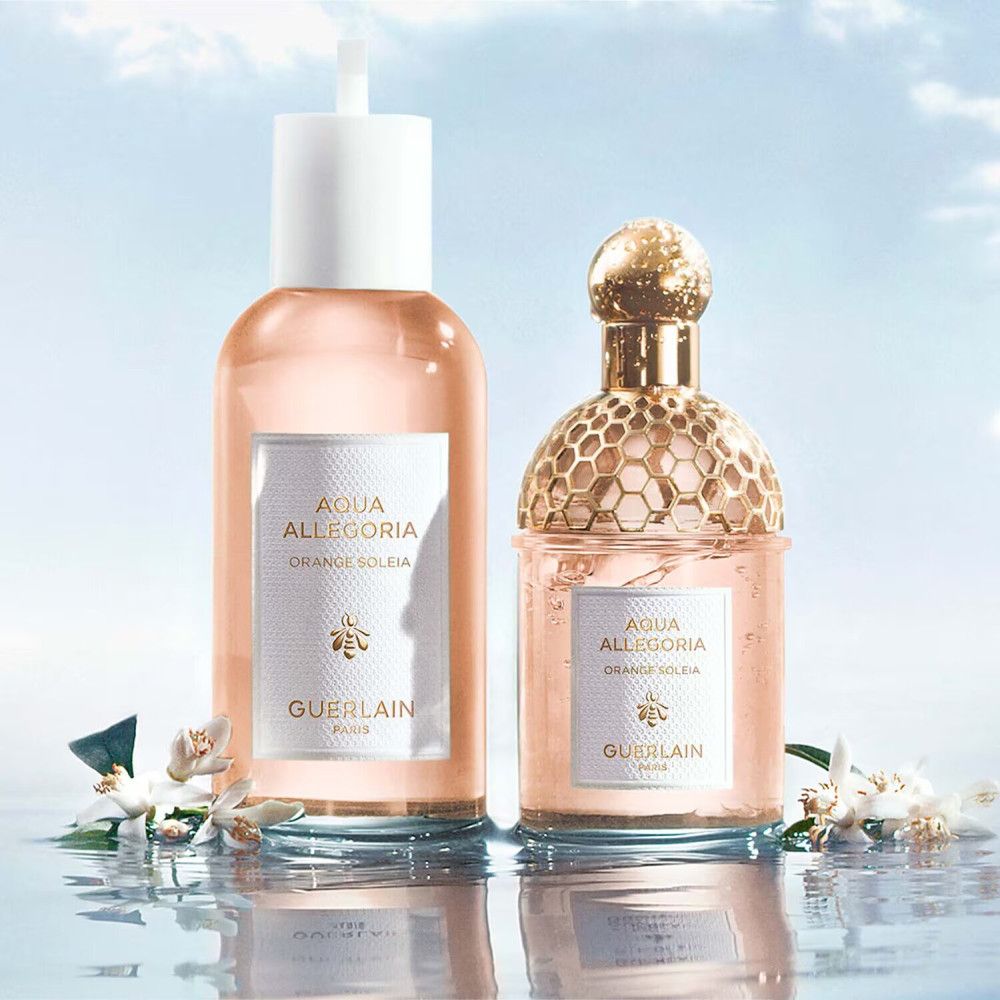 Due flaconi di profumo accanto a fiori. Flaconi con etichette Aqua Allegoria, Orange Soleia e Guerlain. Sfondo: acqua.