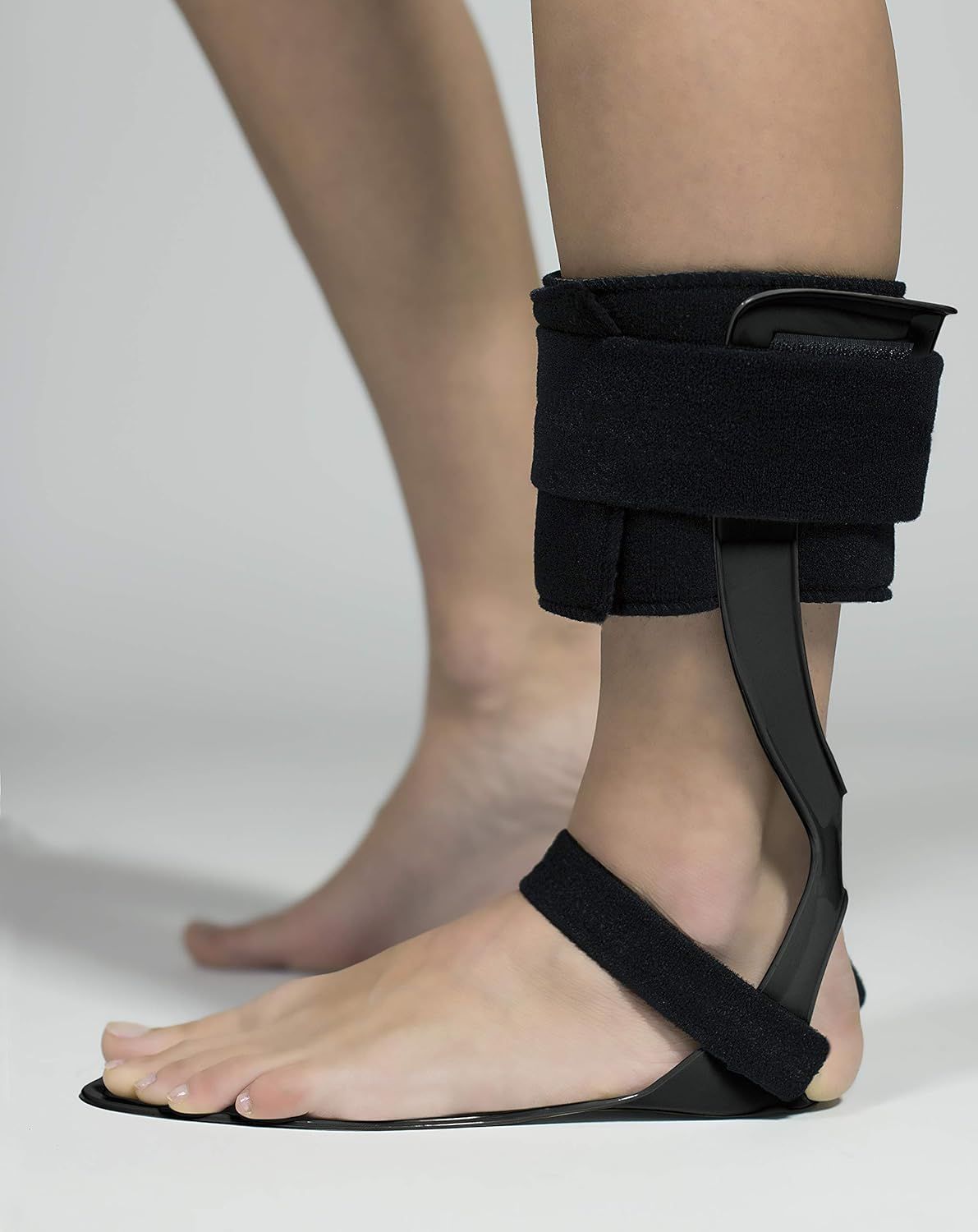 Vista laterale di un tutore di sollevamento del piede nero sul piede sinistro di una persona con chiusura in velcro.