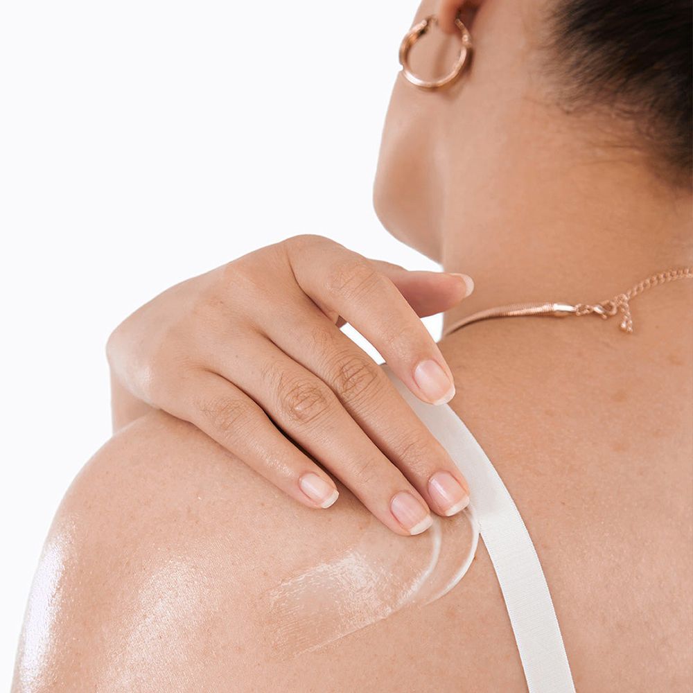 Persona con lozione sulla spalla. Lozione applicata sulla pelle. Top bianco. Collana e orecchino dorati.