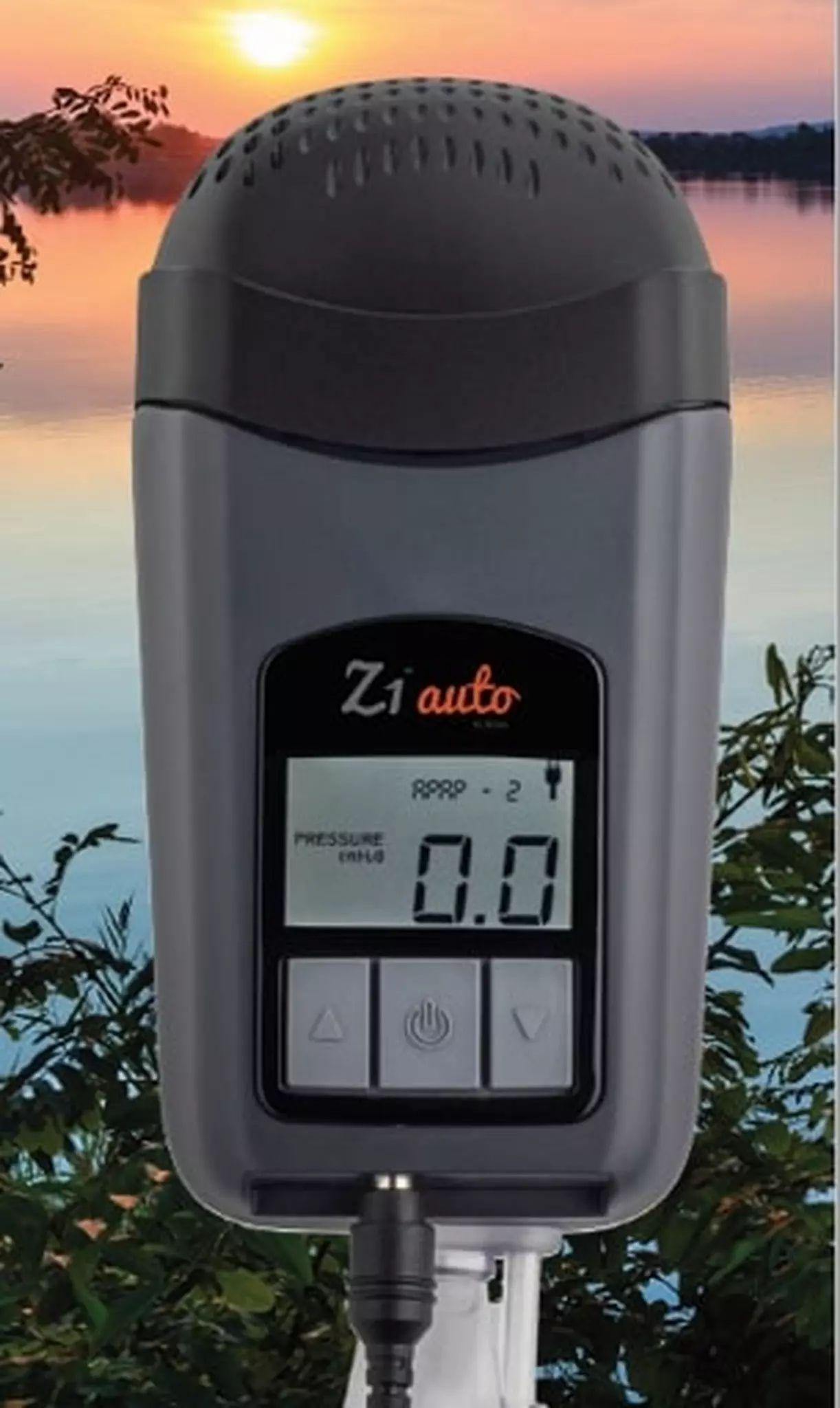Dispositivo CPAP da viaggio grigio con display, mostra "0.0", davanti a lago e alberi.