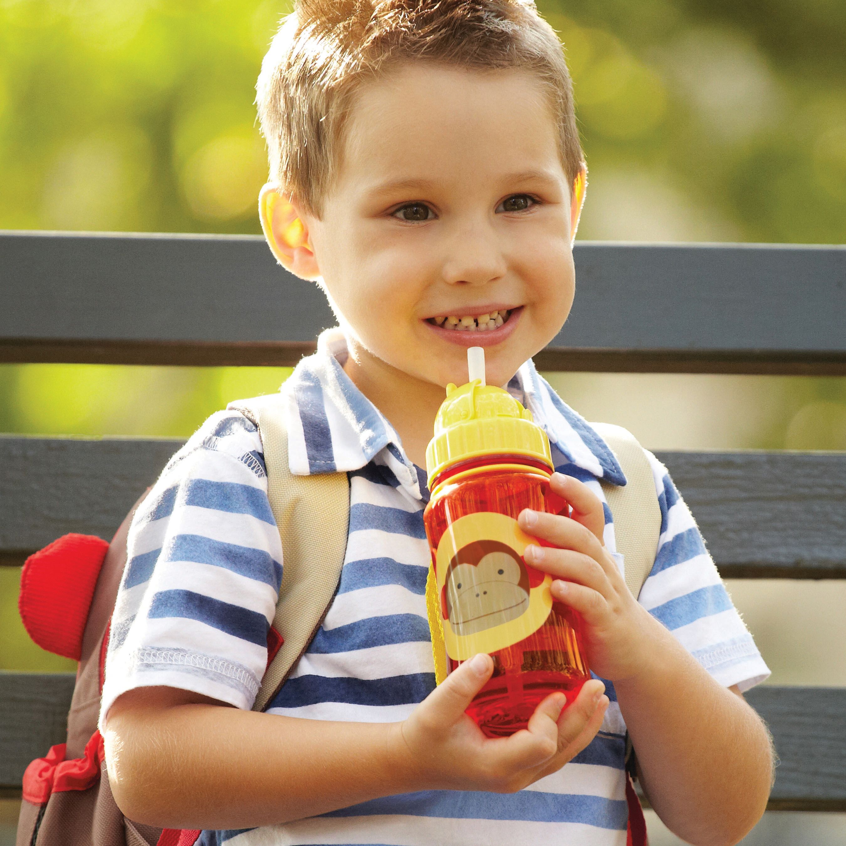 Bambino beve da borraccia rossa con motivo scimmia. Tappo giallo e cannuccia. Il bambino indossa uno zaino.