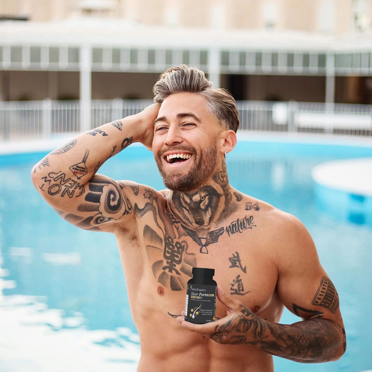 Uomo tatuato a bordo piscina tiene una bottiglia nera di SanaExpert Haar Forte Gold Pro Man. Sorride.