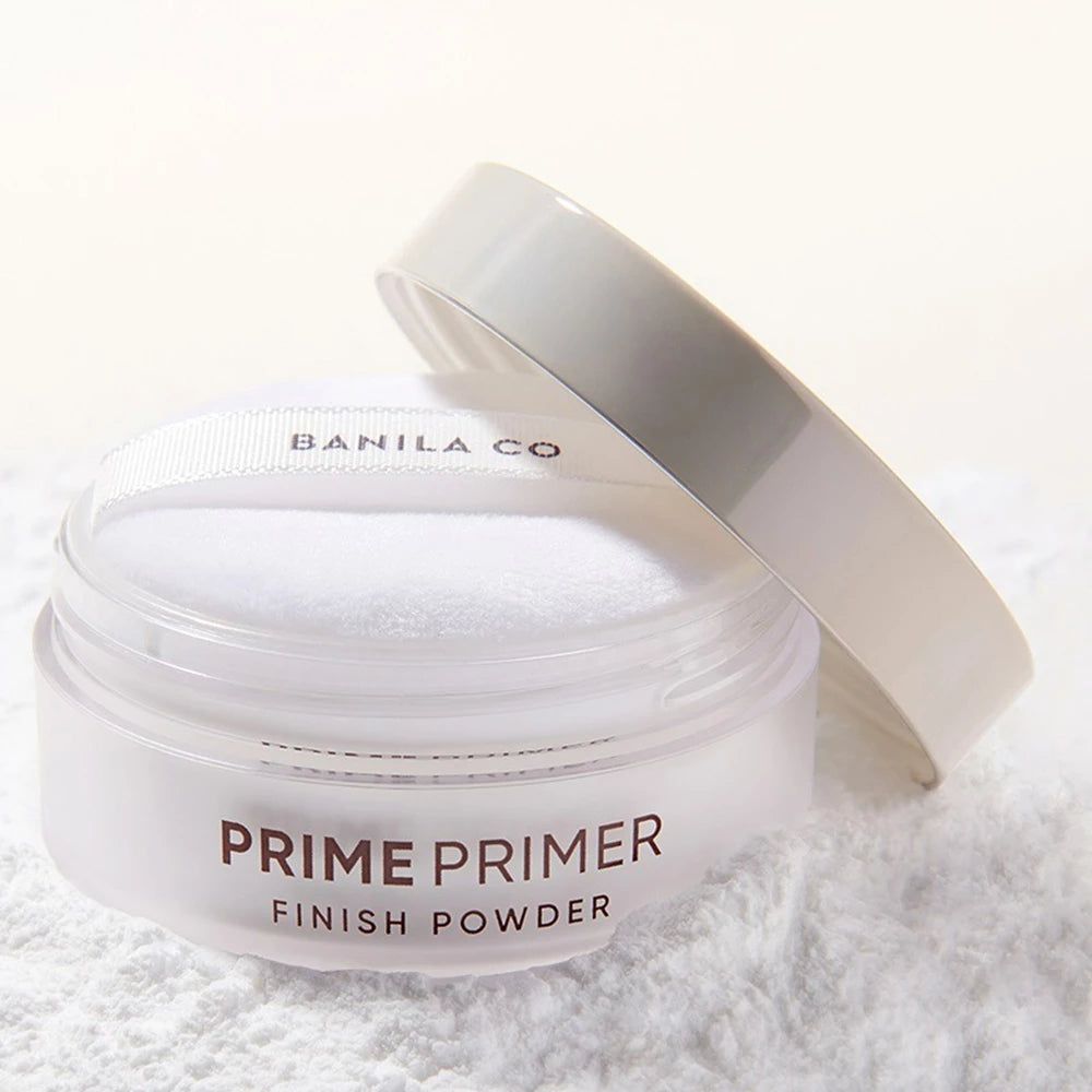 Vasetto bianco con coperchio e piumino. Scritta: PRIME PRIMER FINISH POWDER. Polvere su sfondo bianco.