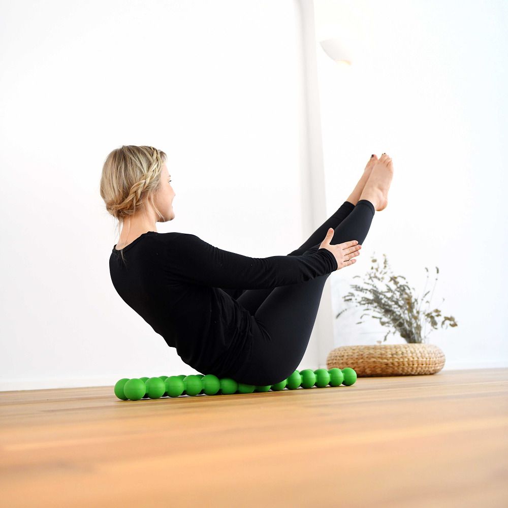 Una donna esegue un esercizio su uno Spinefitter verde. Lo sfondo è chiaro e in legno.