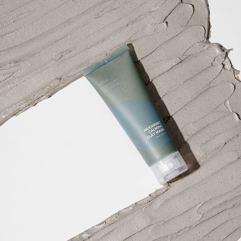 Tubo verde su argilla grigia. Scritta: Mugwort Calming Clay Mask. Nome del prodotto e marchio visibili.