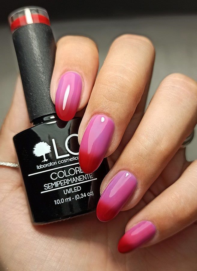 Mani con unghie sfumate rosso/rosa. Flacone smalto con scritta: LCI, Colore Semipermanente.