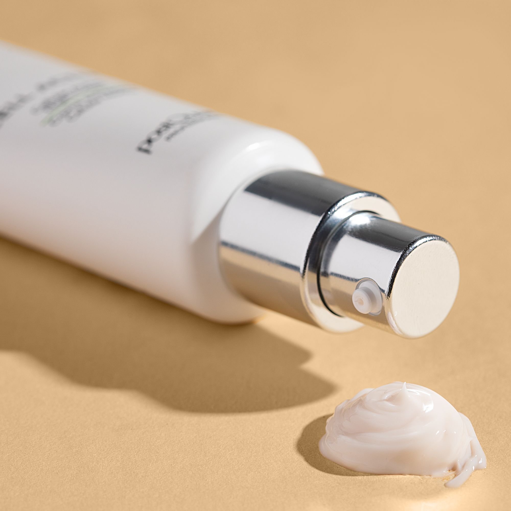 Flacone bianco con erogatore argentato. Macchia di crema su sfondo beige.