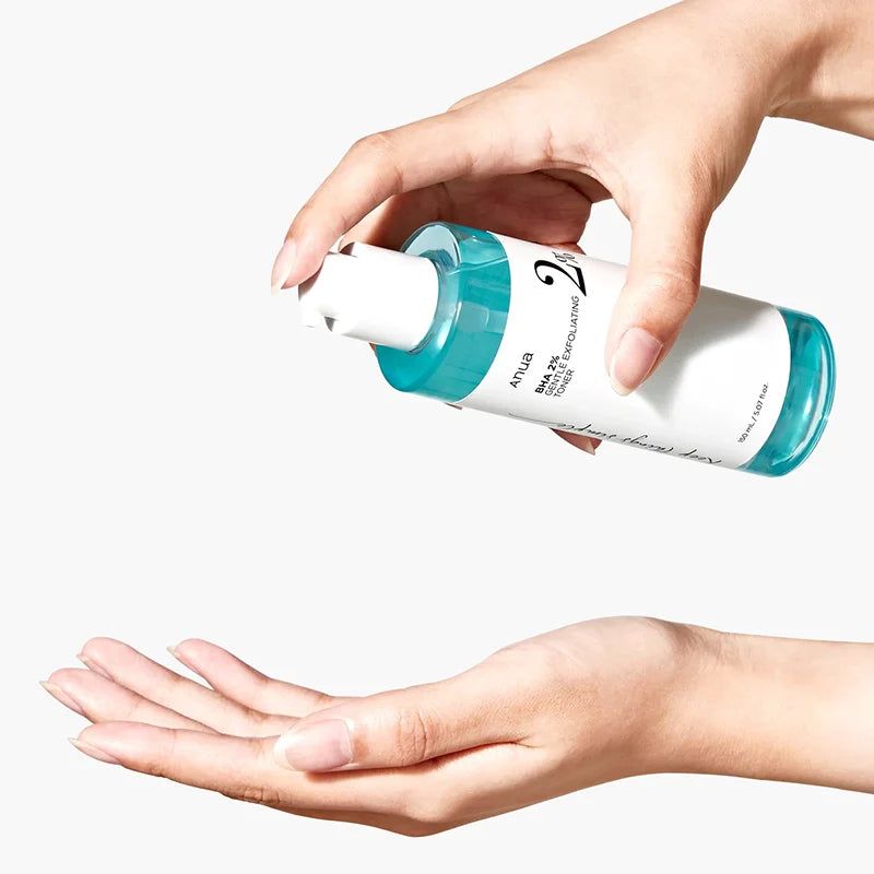 Mani che tengono un flacone di toner. Scritta: Anua BHA 2% Gentle Exfoliating Toner. Liquido versato nel palmo.